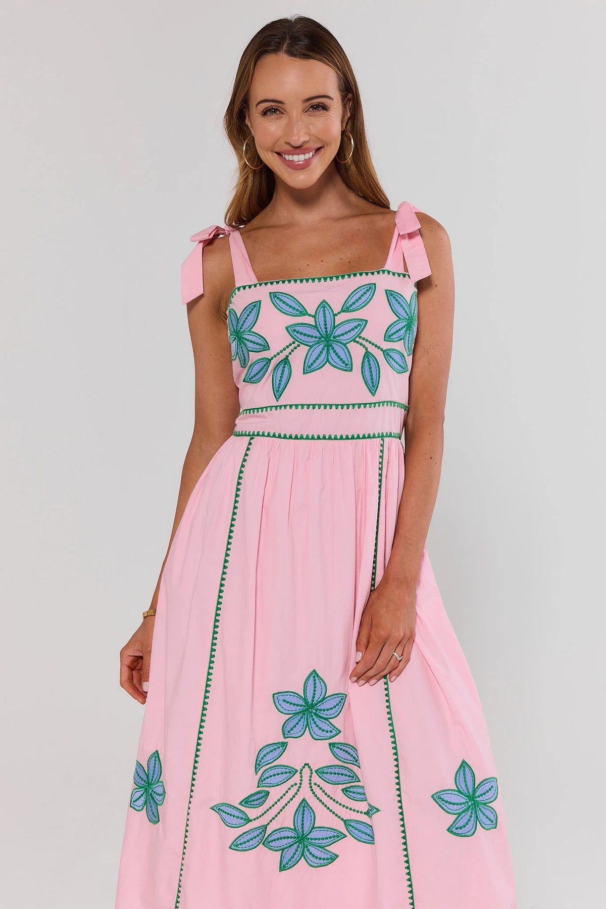 Woman wearing a pink dress with floral embroidery on a gray background