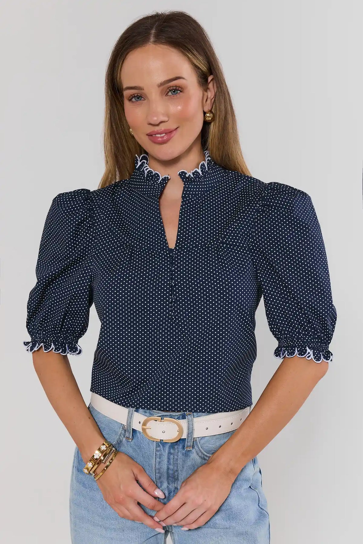 Woman wearing navy polka dot puff sleeve blouse with white ruffle trim, styled with jeans - Front View | Avara