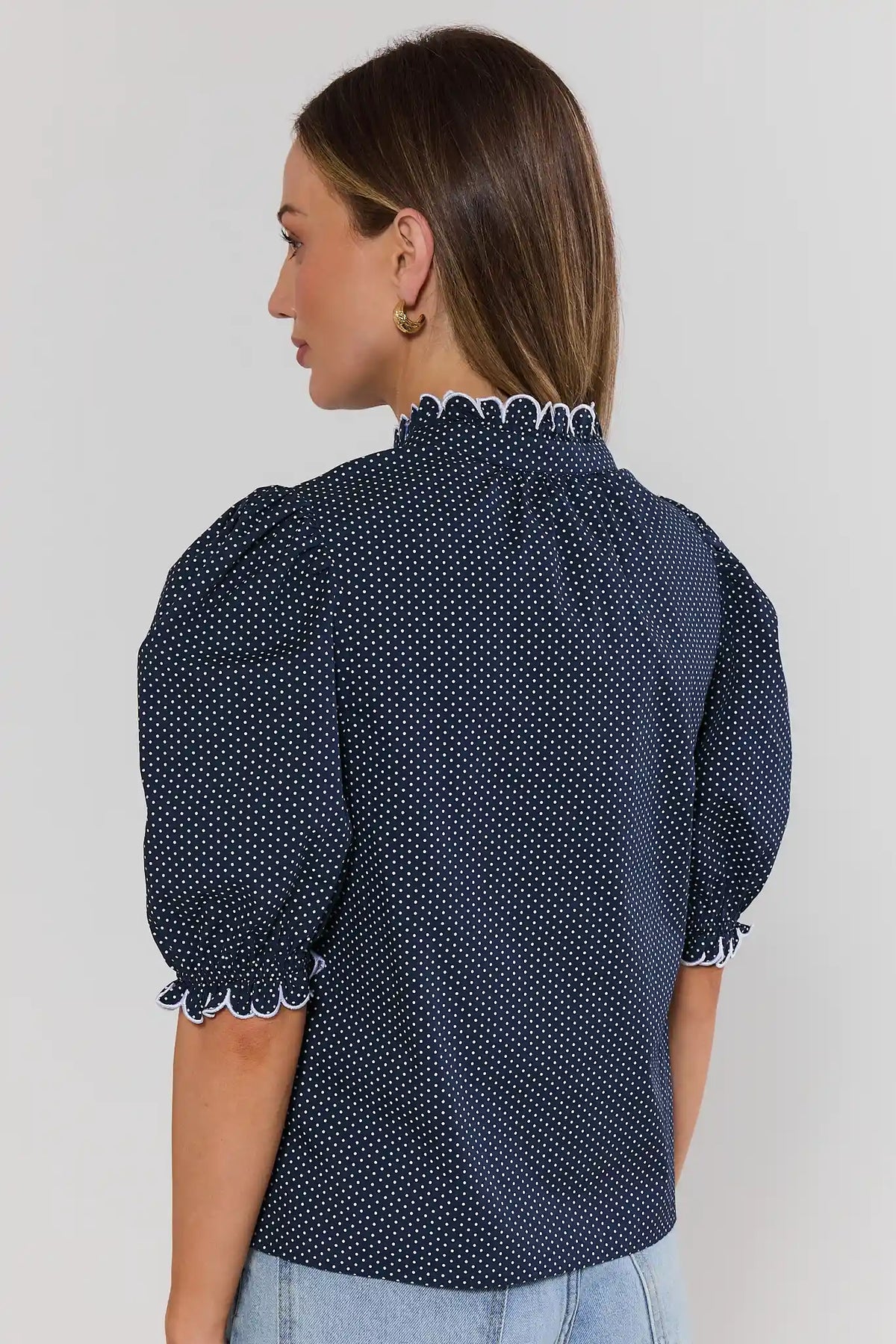 Back view of navy polka dot blouse with white ruffle collar and scallop-trimmed puff sleeves | Avara