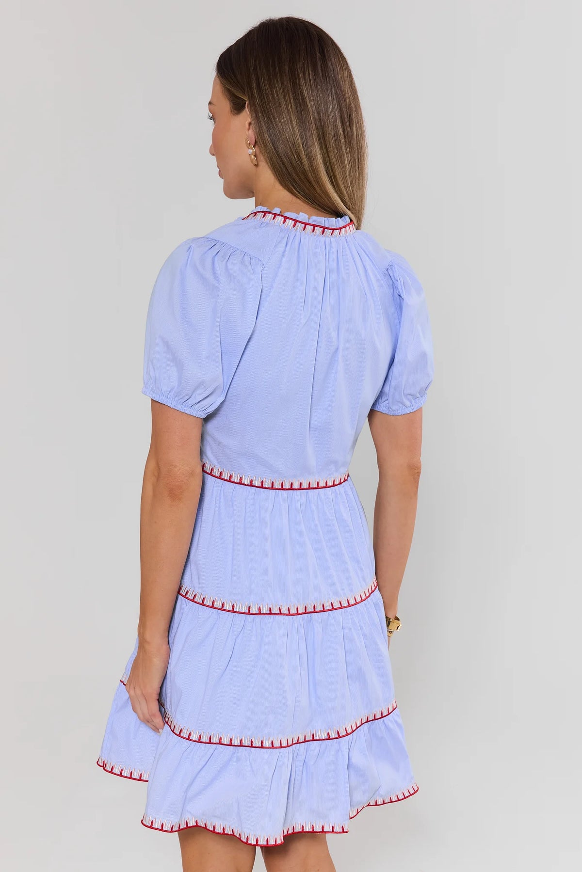 Woman standing wearing a light blue dress with red trim on a plain background