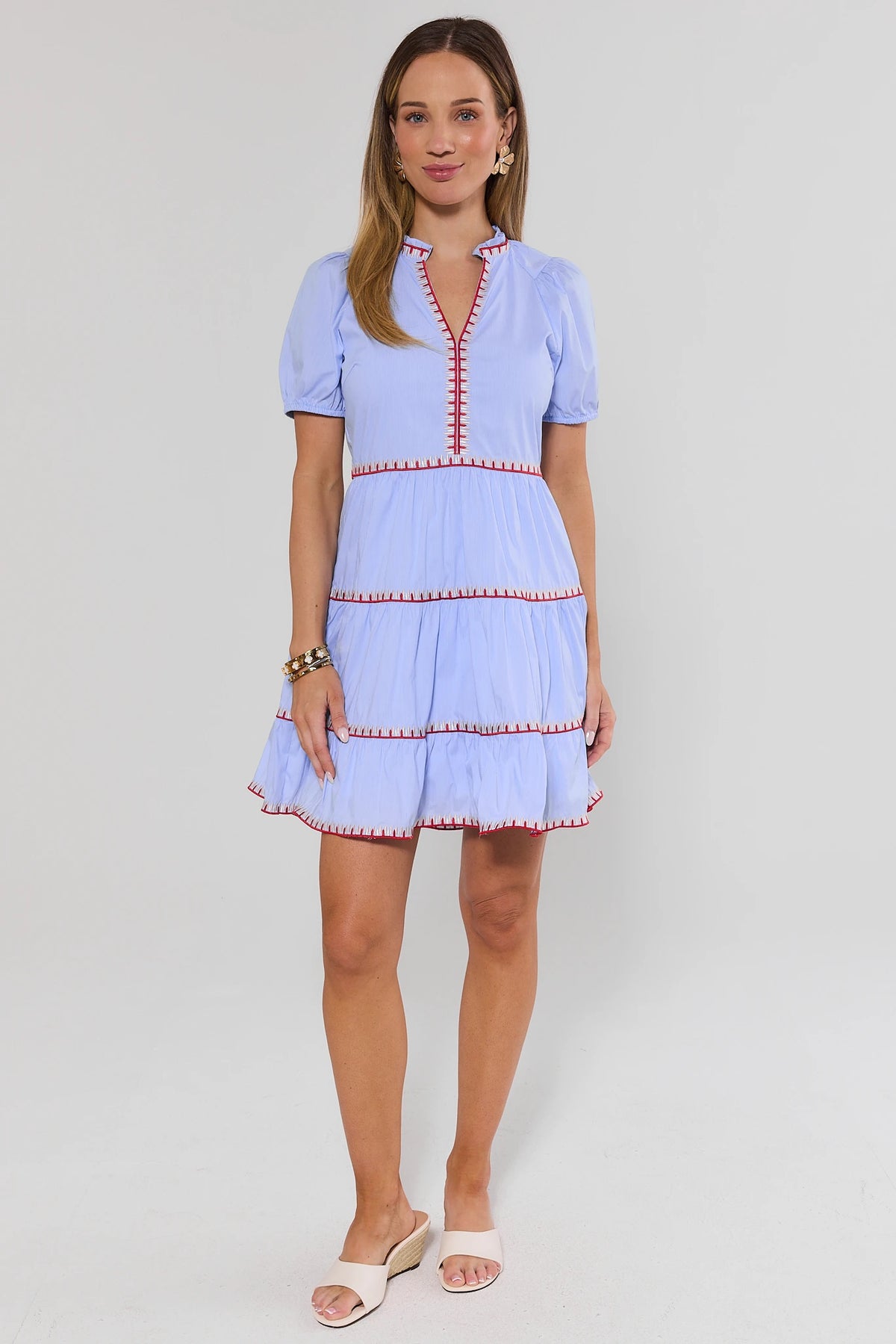 Woman wearing a light blue dress with red trim on a white background stand