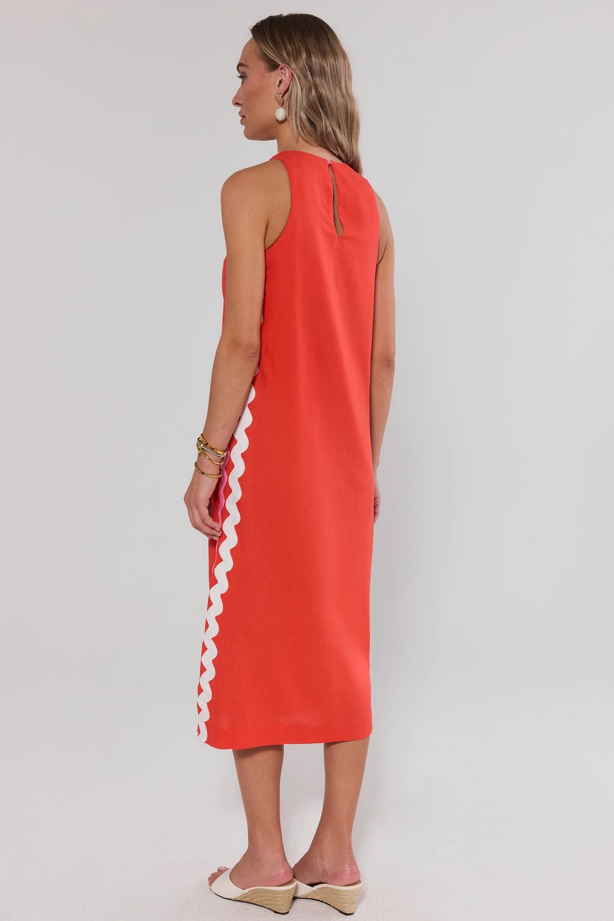 Woman standing wearing a red dress with white trim on a plain background