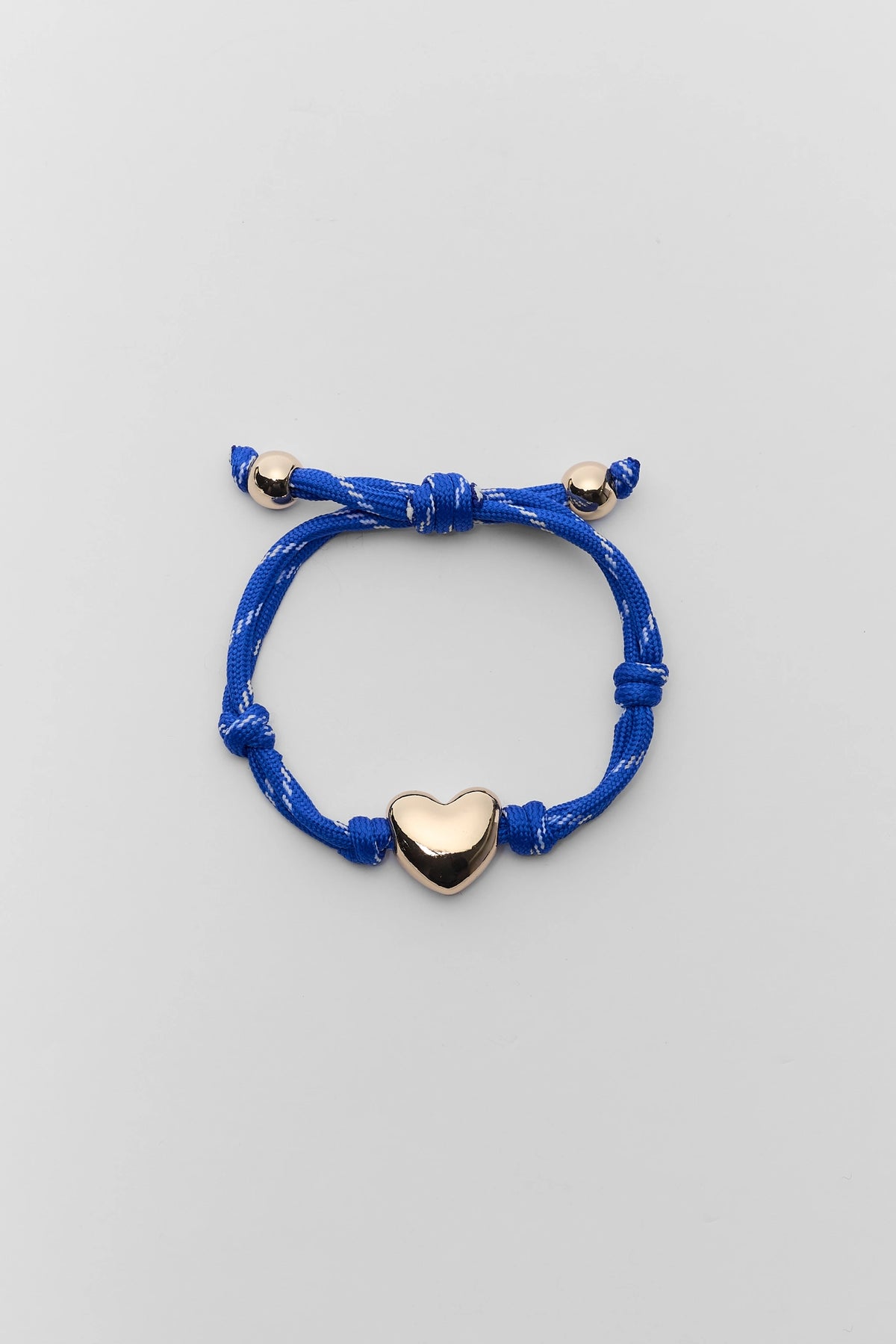Blue paracord heart charm bracelet with gold-tone heart bead and adjustable cord - Flat Lay | Avara