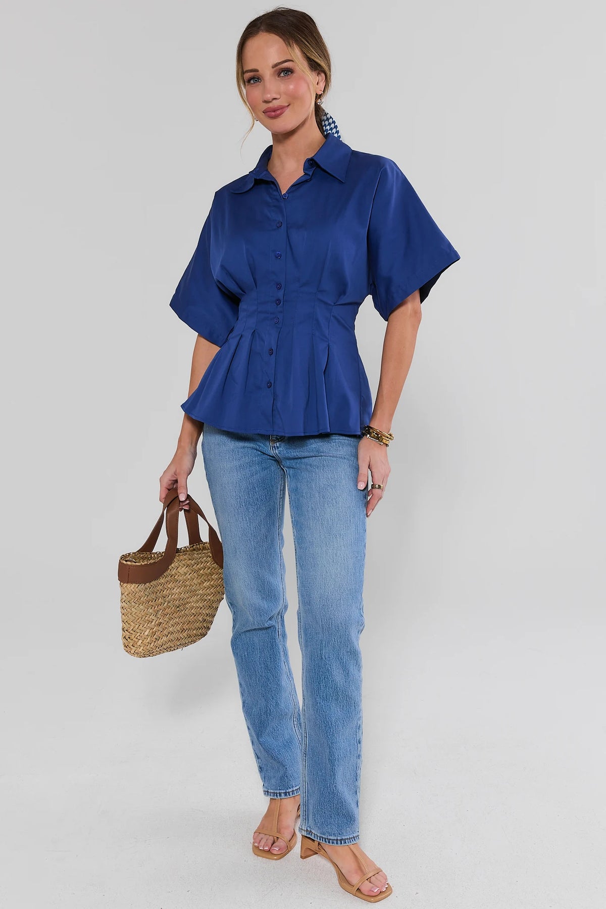 Woman wearing blue pleated button up top with jeans and straw bag, full length styled look | Avara