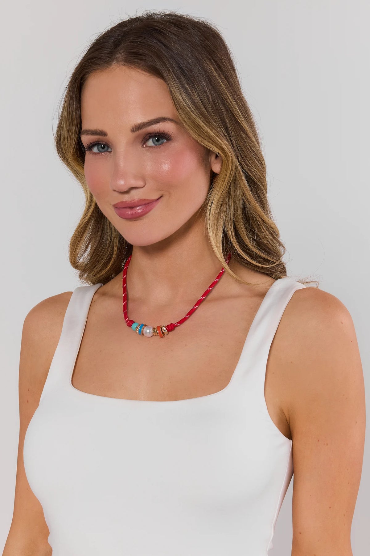 Woman wearing a white tank top and a red beaded necklace against a plain background