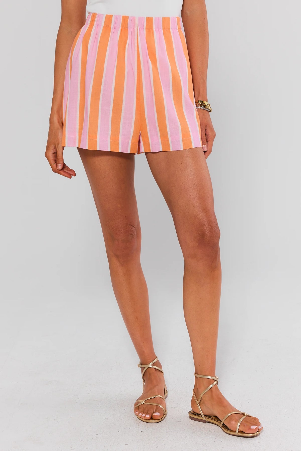 Pink and orange striped elastic waist shorts on model with gold sandals, front view | Avara