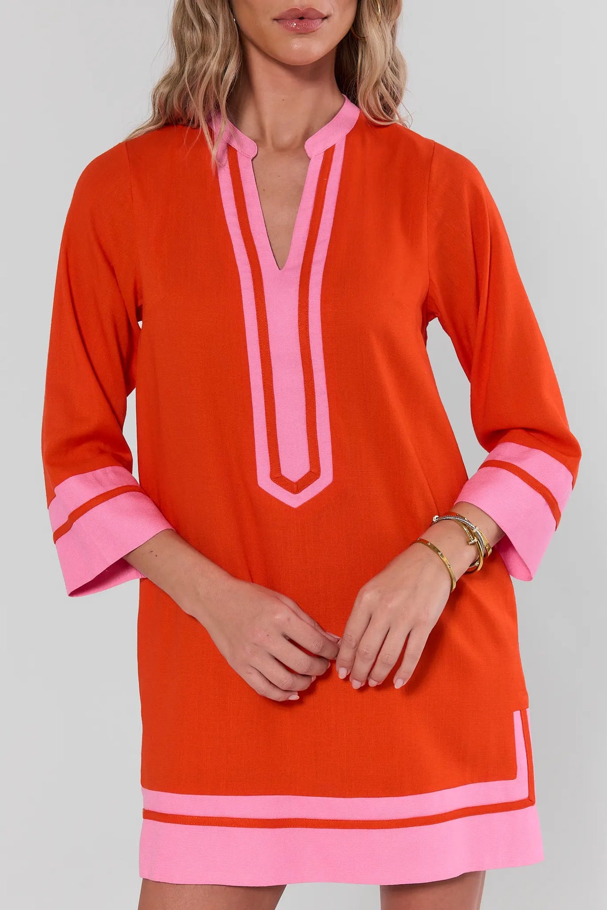 Orange tunic dress with pink contrast trim and V-neckline, close-up front detail on model | Avara