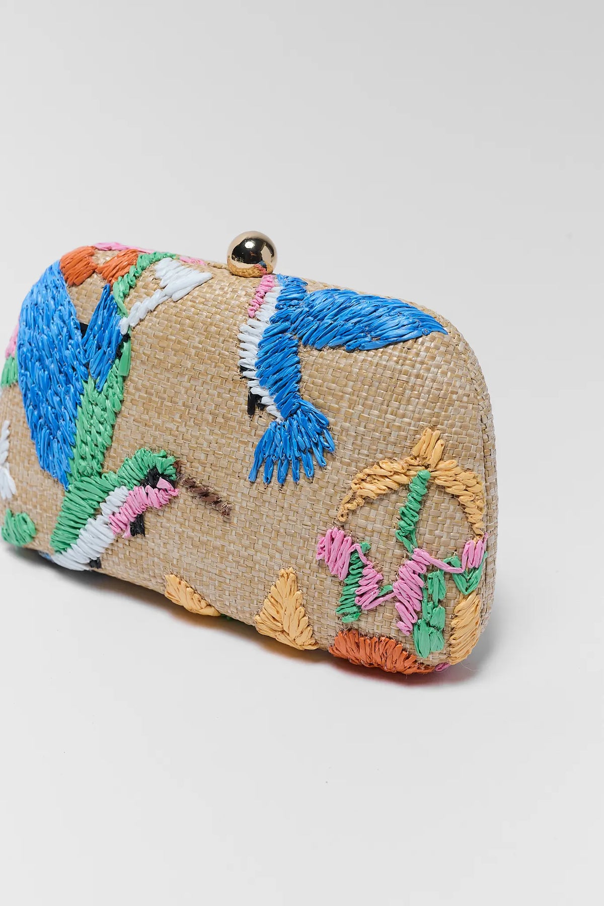 Beige handbag with colorful embroidered designs on a light gray background close up
