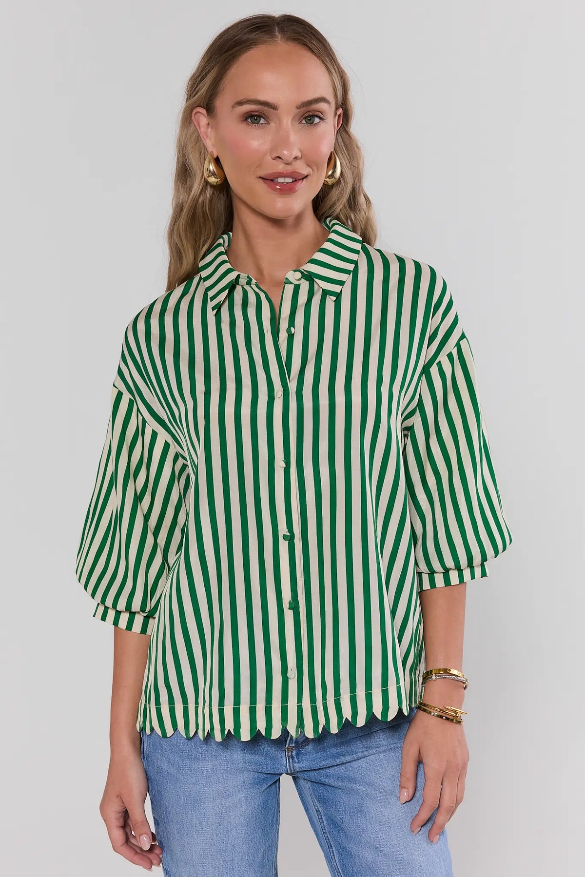 Woman wearing green striped button-up top with scallop hem over blue jeans - Front View | Avara