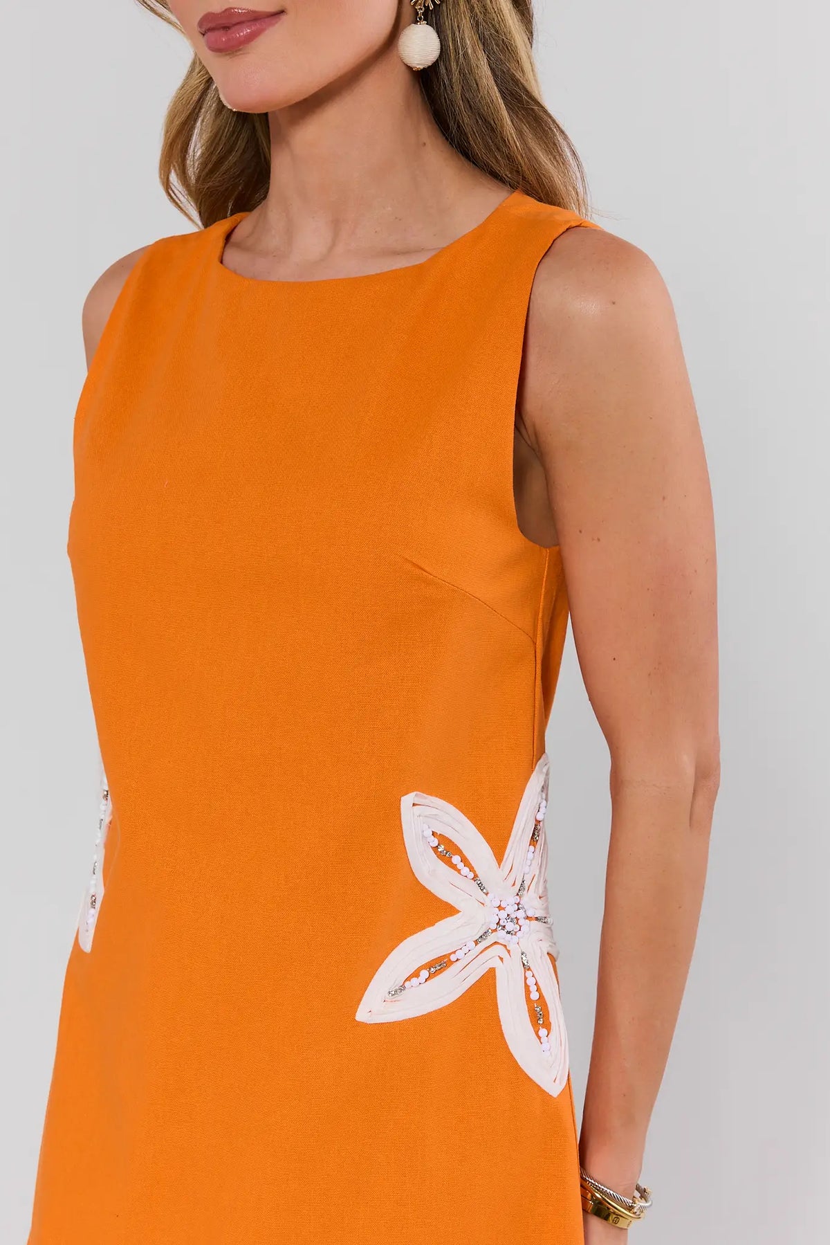 Orange embroidered dress close-up showing white beaded floral detail and high scoop neckline on model | Avara