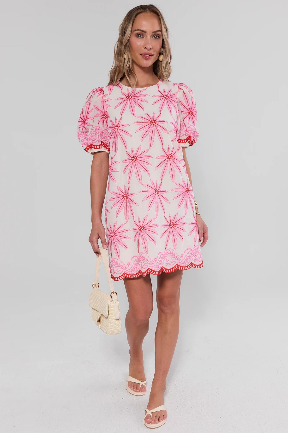 Woman wearing a pink and white dress with floral pattern on a gray background standing