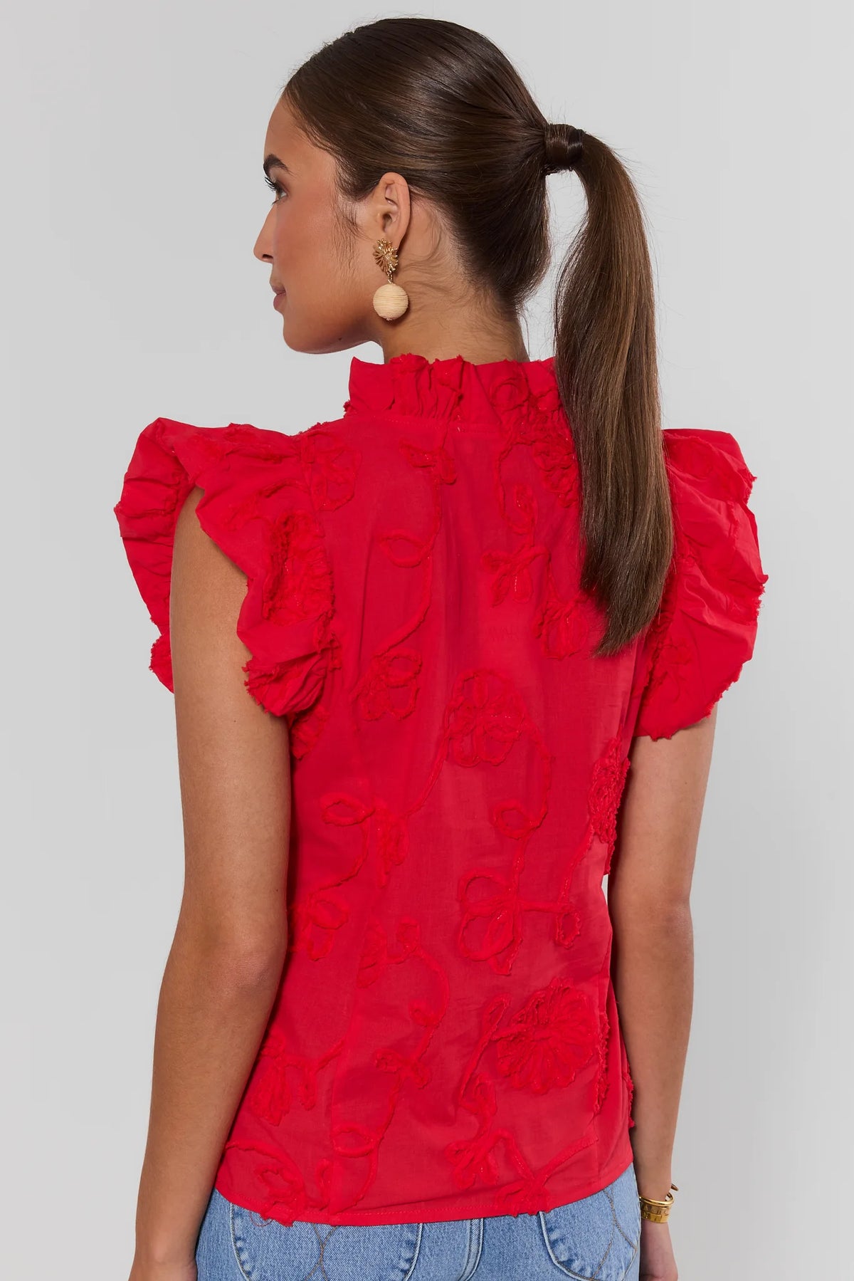 Woman standing wearing a red blouse with ruffled sleeves on a plain background