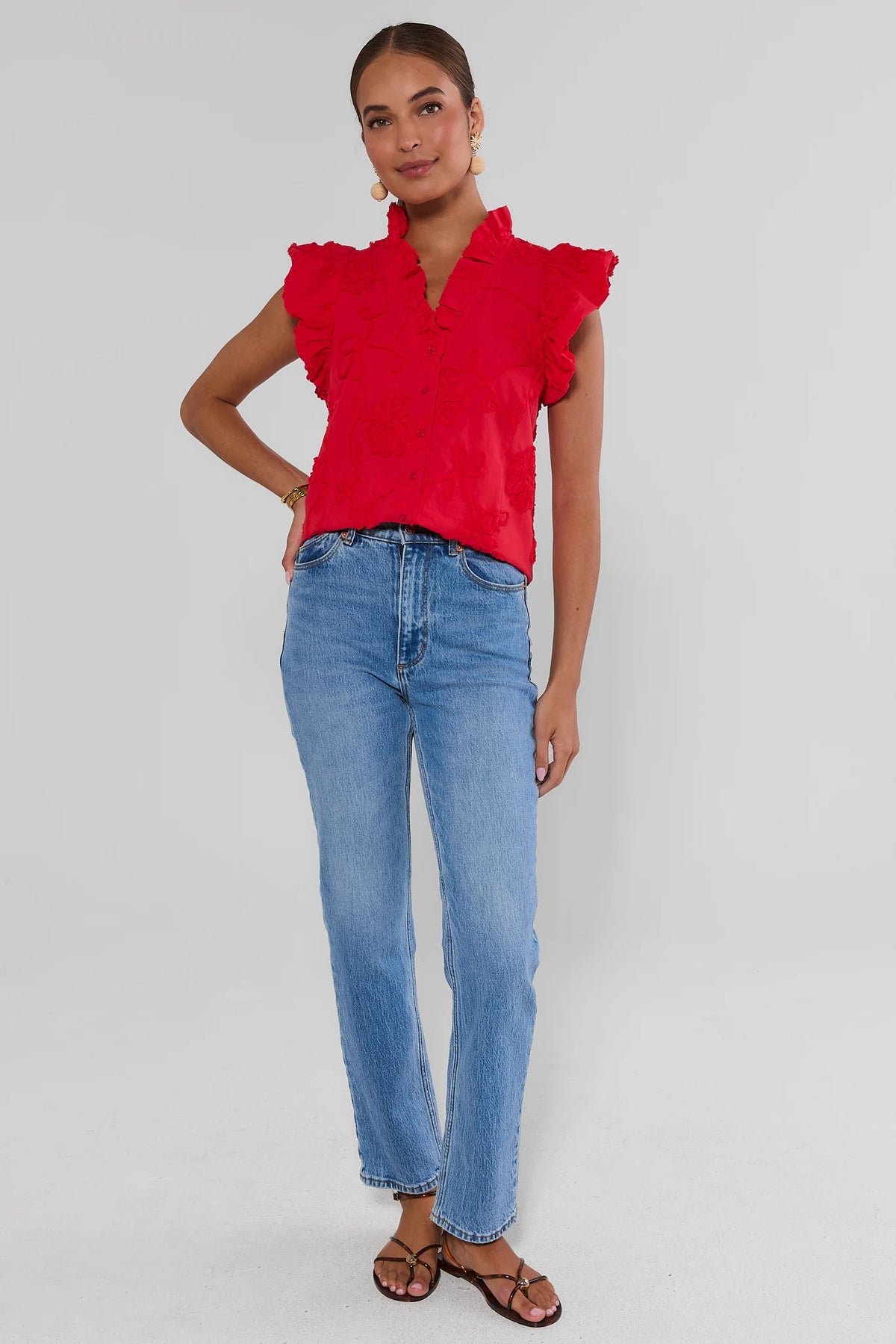 Woman wearing a red blouse with ruffled sleeves and blue jeans on a gray background