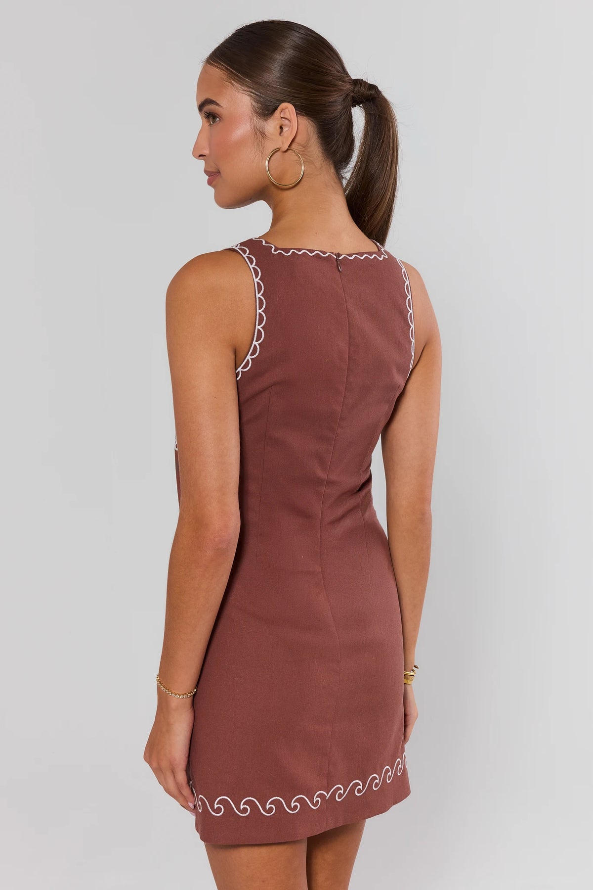 Back view of brown shell embroidered short dress showing zipper closure and white wave trim hem | Avara