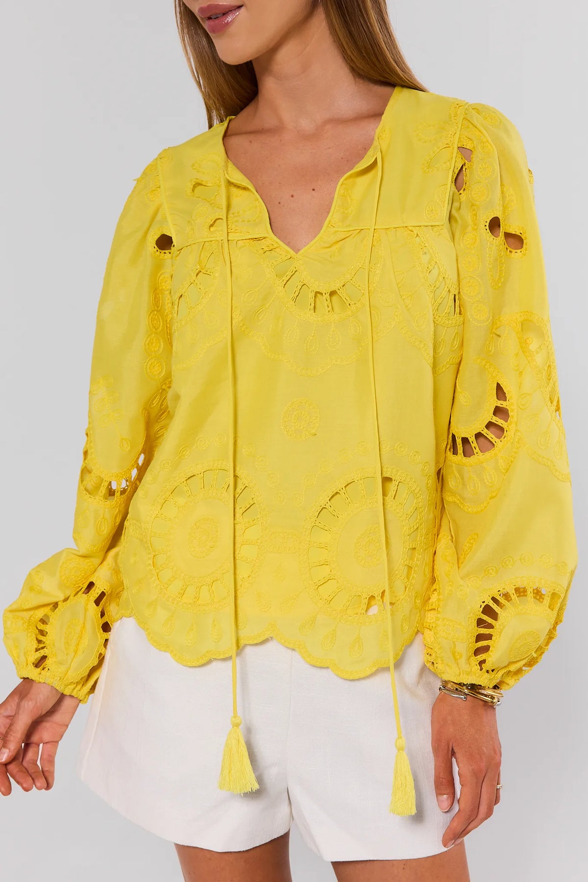 Yellow eyelet blouse close-up showing scalloped hem, cutwork detailing, and tassel split neckline | Avara