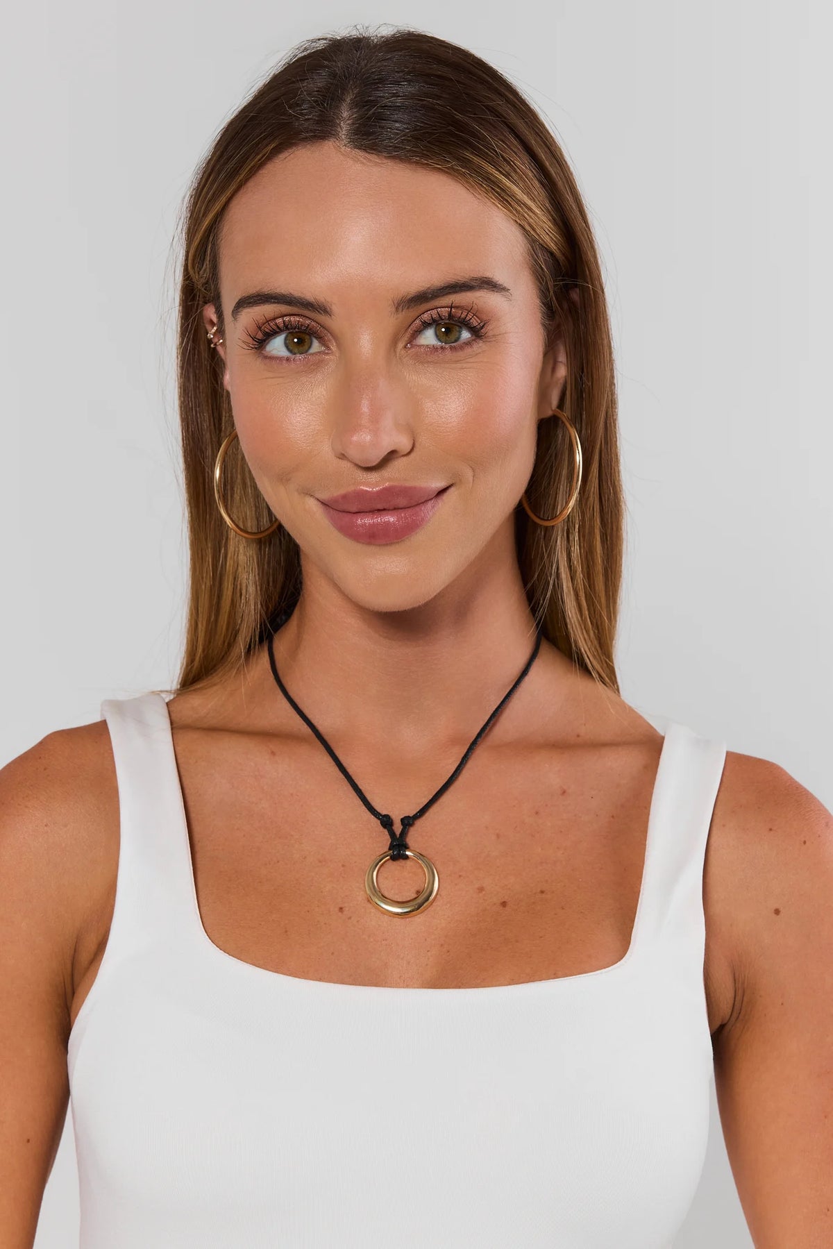 Woman wearing black cord circle pendant necklace with gold hoop earrings over white tank top - On Model | Avara