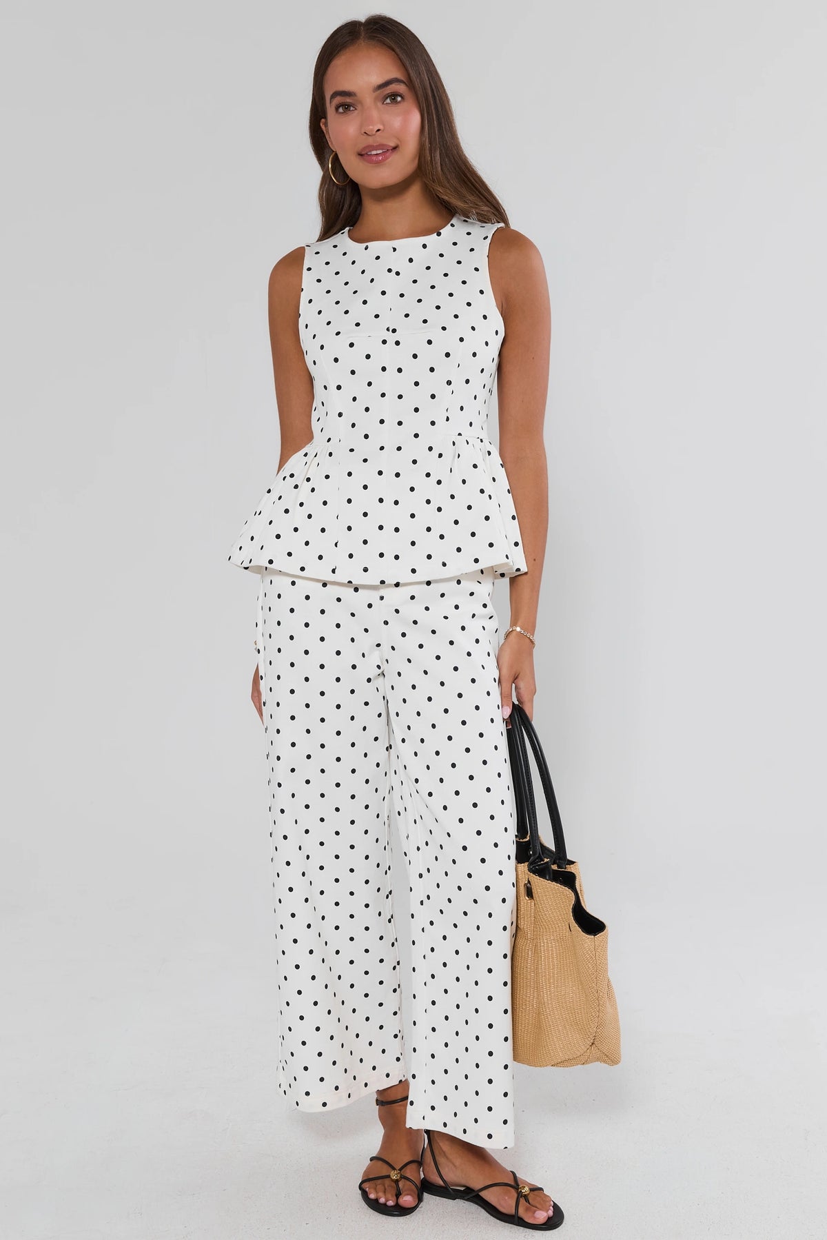 White polka dot wide leg pants styled with matching peplum top and rattan bag - Full Length On Model | Avara