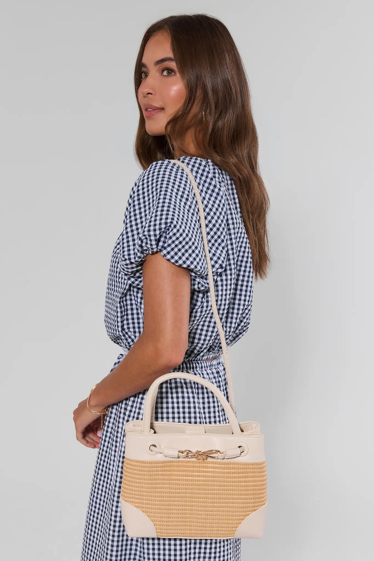 Woman in gingham dress holding tan raffia white trim bag with crossbody strap - Side On Model | Avara