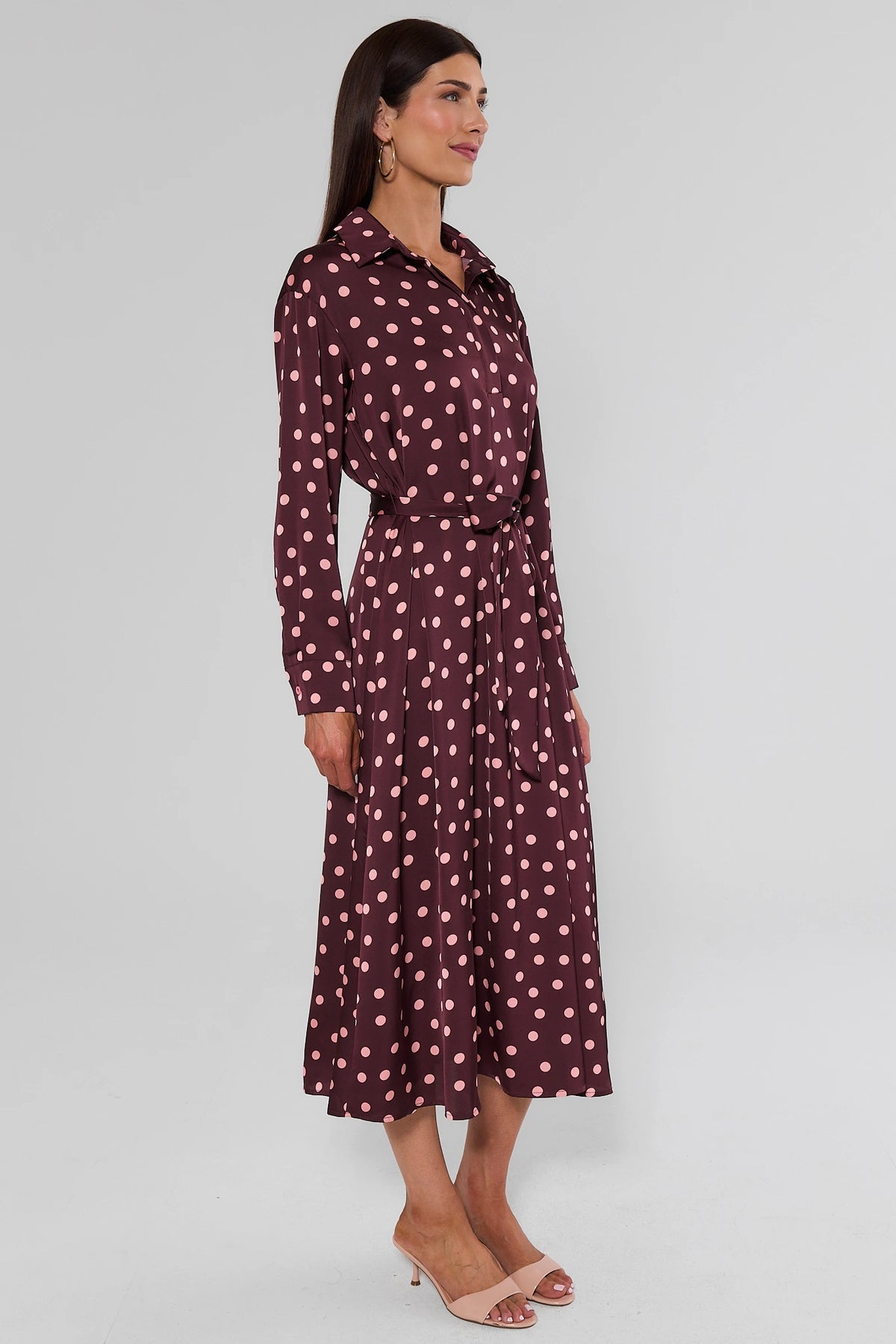 Side profile of brown polka dot midi dress showing flowy skirt, long sleeves, and tie waist on model | Avara