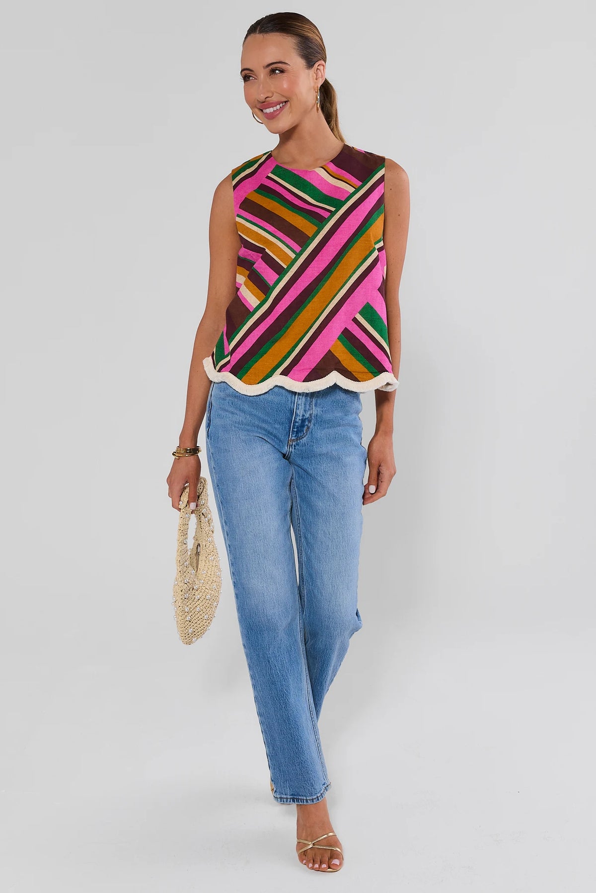 Woman walking Gabby Multi Striped Fringe Trim Tank Top with light wash jeans and gold hoop earrings on white background
