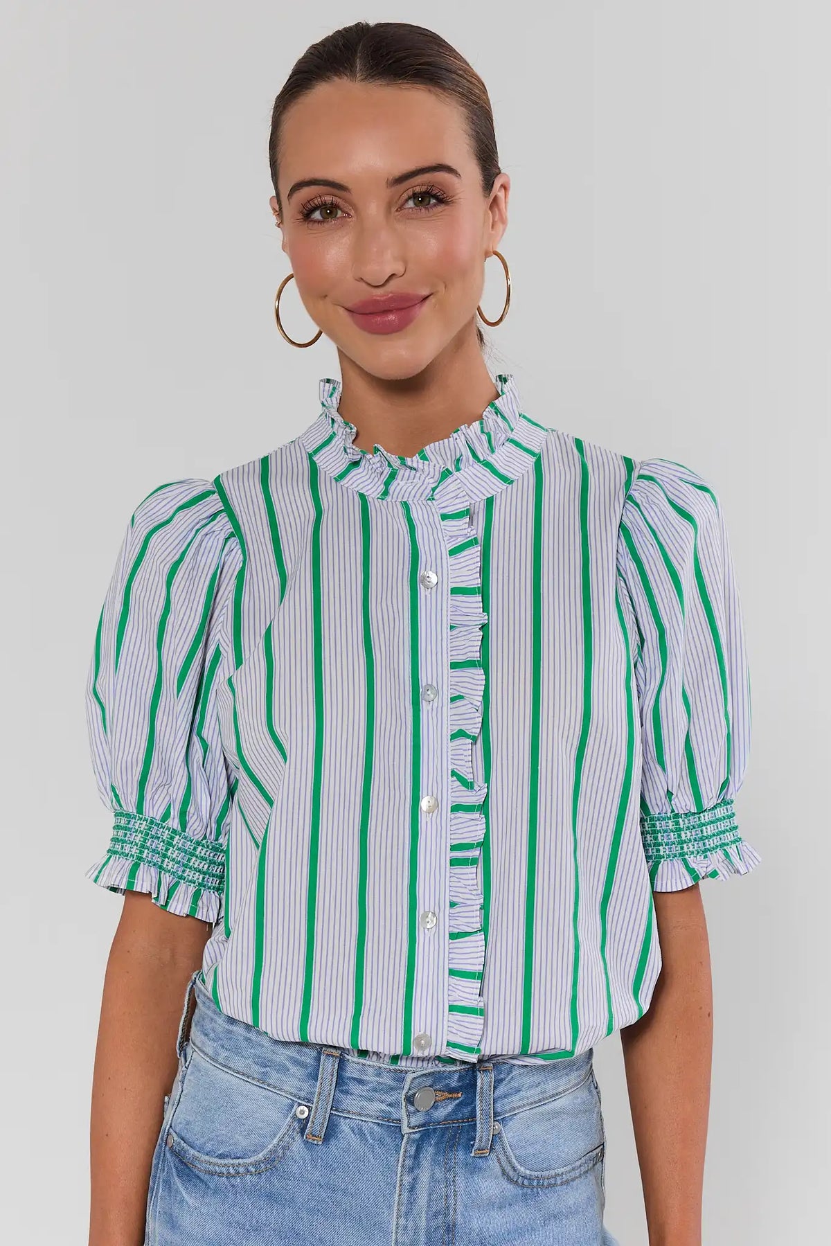Woman wearing green striped ruffle button-up top with smocked cuffs, front view on model | Avara