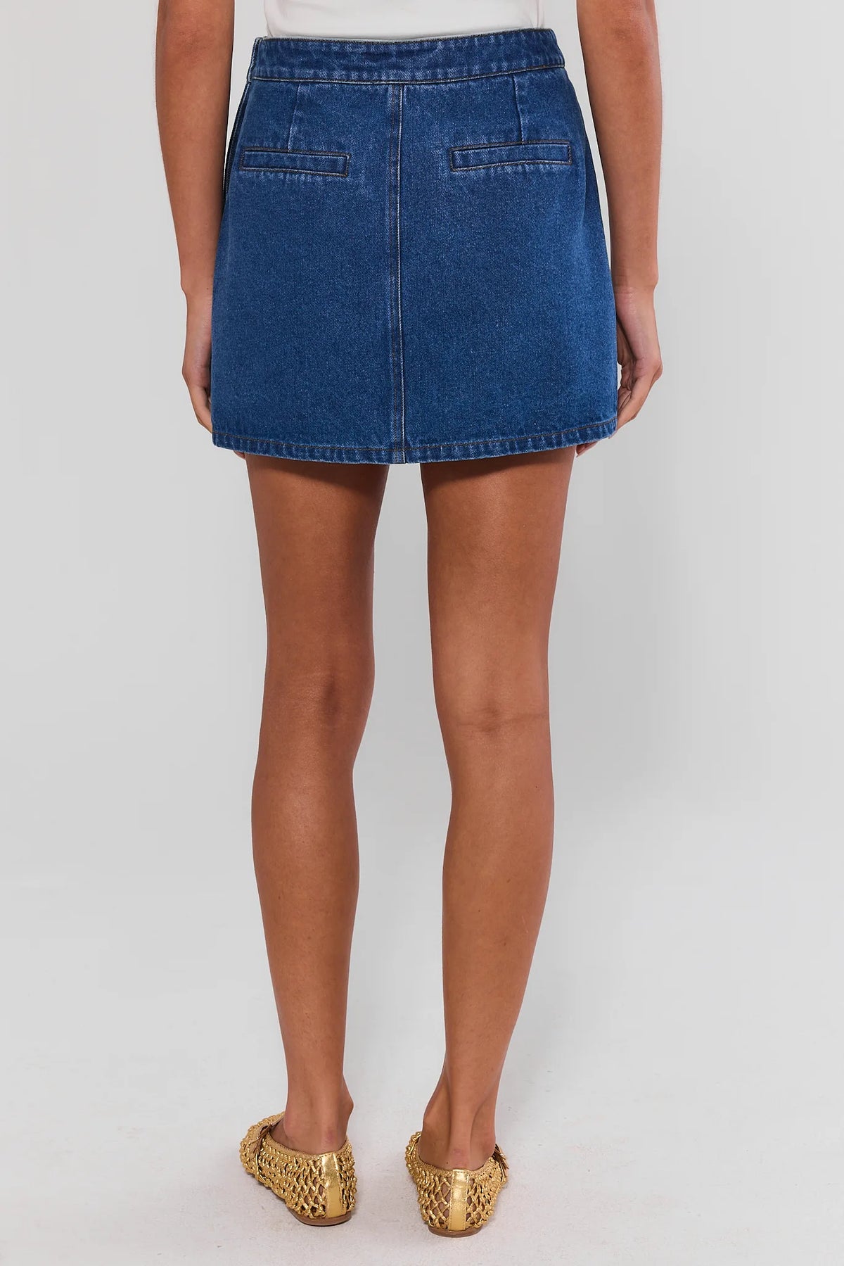 Back view of blue Vickie Denim Button Up Skirt with slit hem detail, paired with woven gold flats | Avara