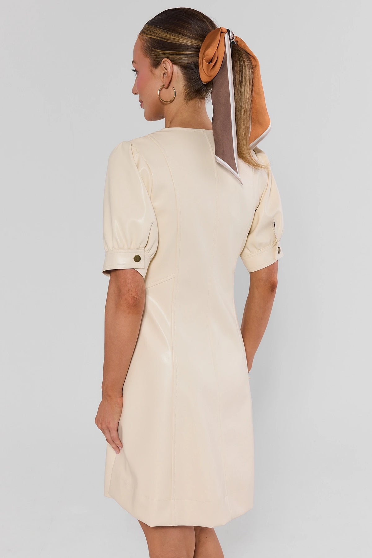 Woman wearing Ivory Faux Leather Short Dress with hair scarf - Back View showing puff sleeves, gold cuff snaps | Avara