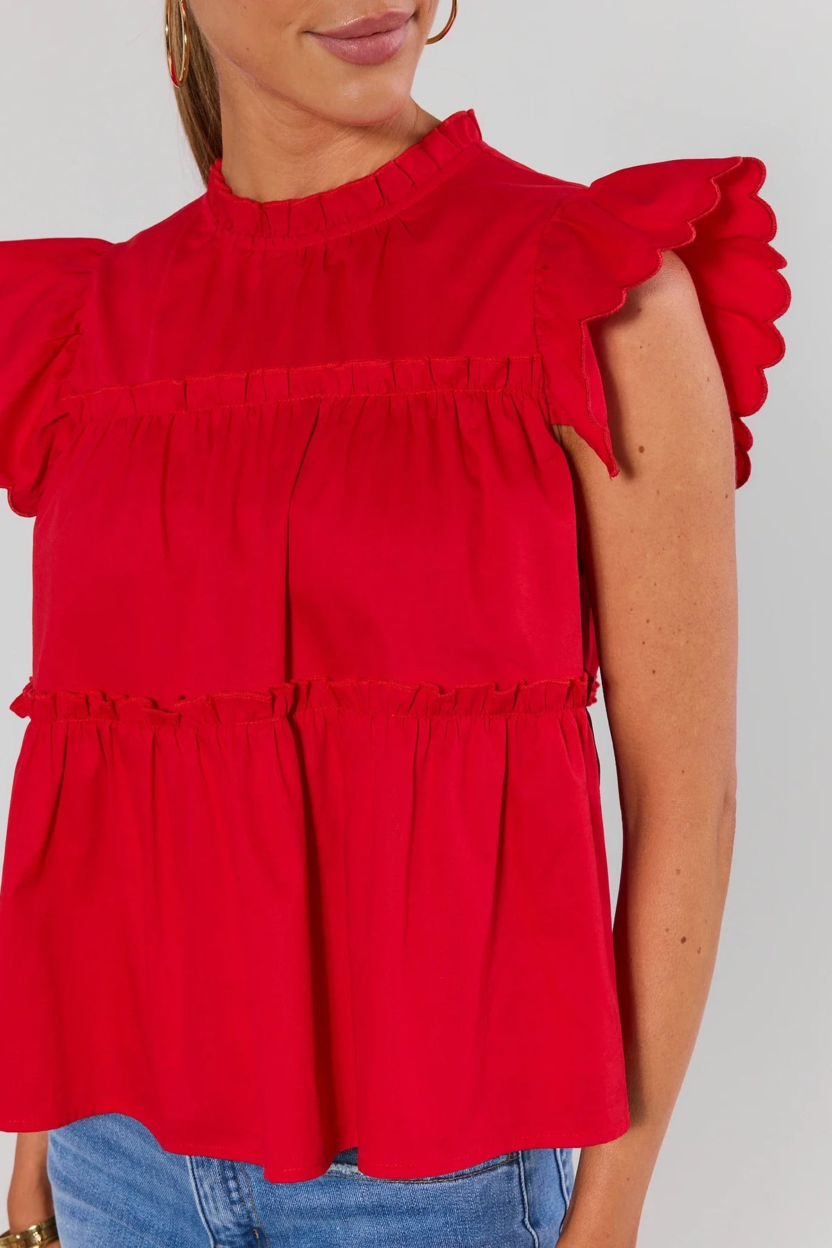 Close-up of red flutter sleeve top showing scalloped ruffle sleeves and tiered bodice detail | Avara