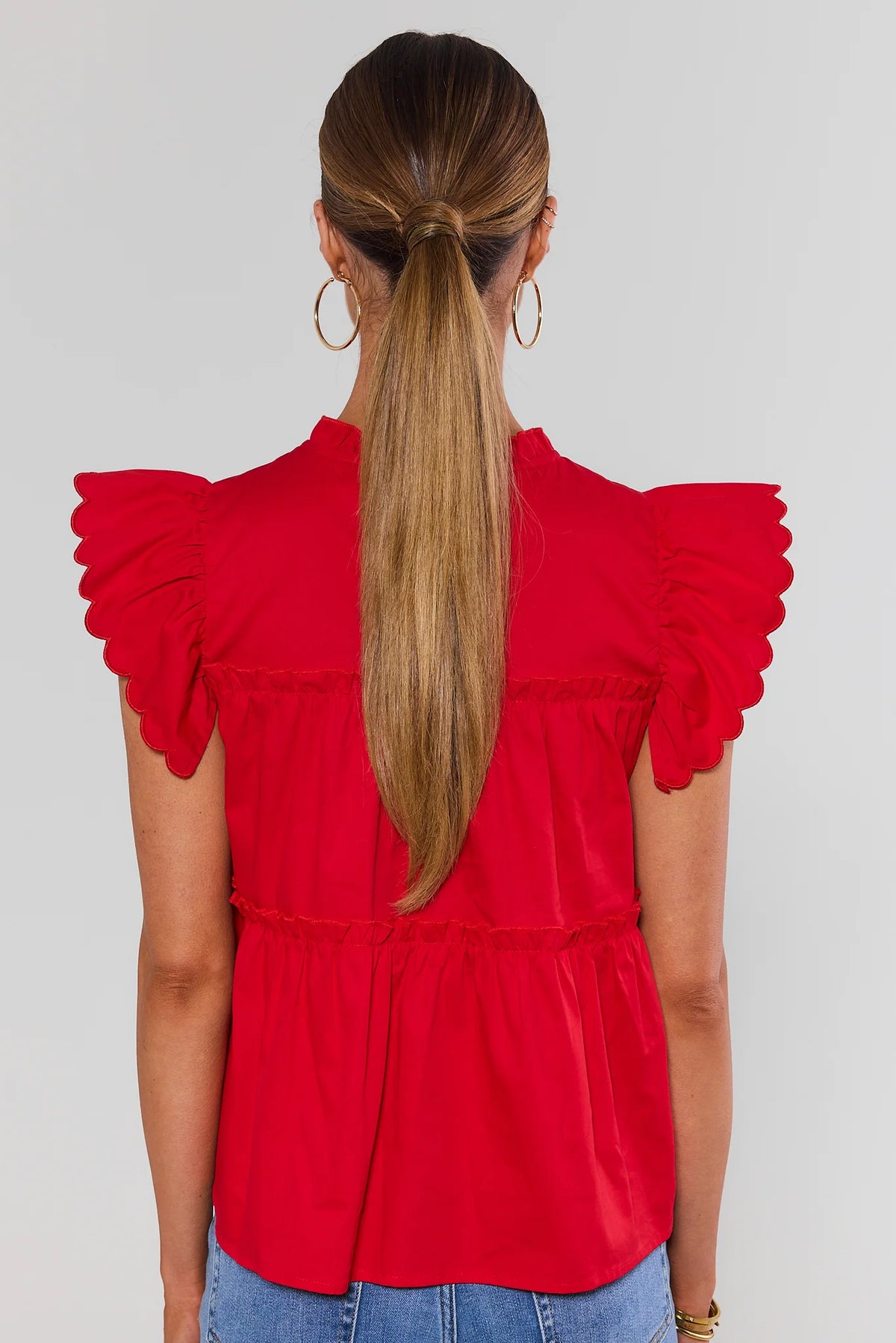 Back view of red tiered flutter sleeve top with scalloped ruffle sleeves and tiered waist detail | Avara