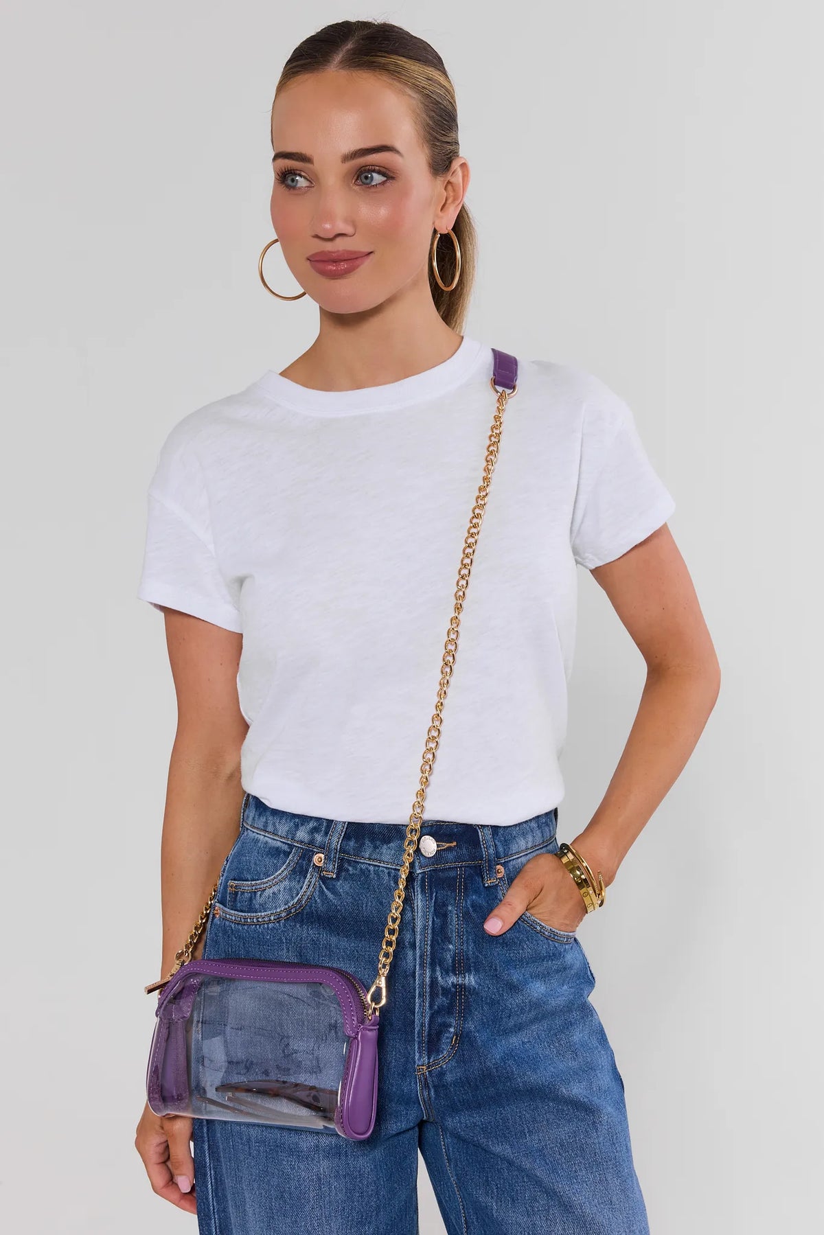 Woman in white tee and jeans wearing clear purple crossbody bag with gold chain - On Model | Avara