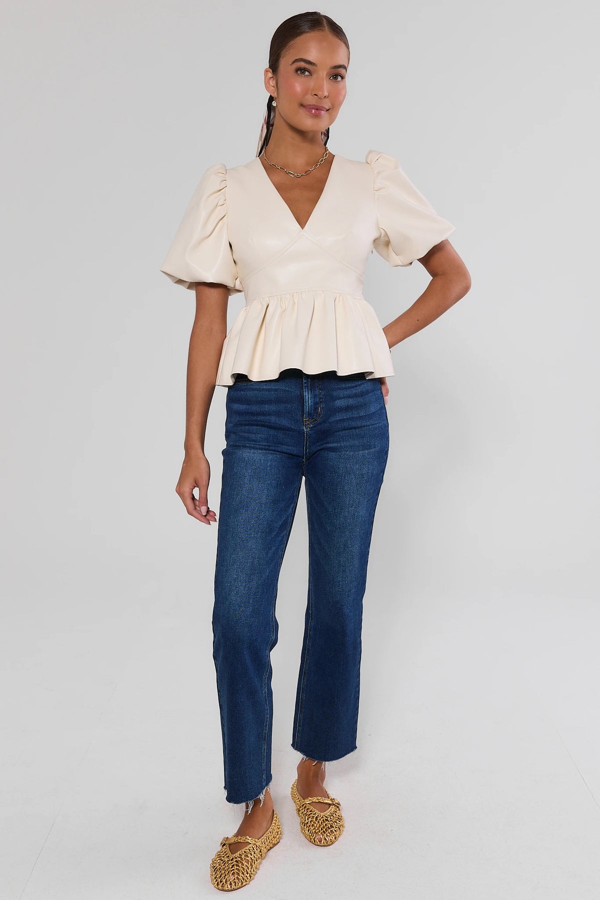 Ivory faux leather peplum top with puff sleeves and V-neckline, worn with blue jeans - Side Profile | Avara