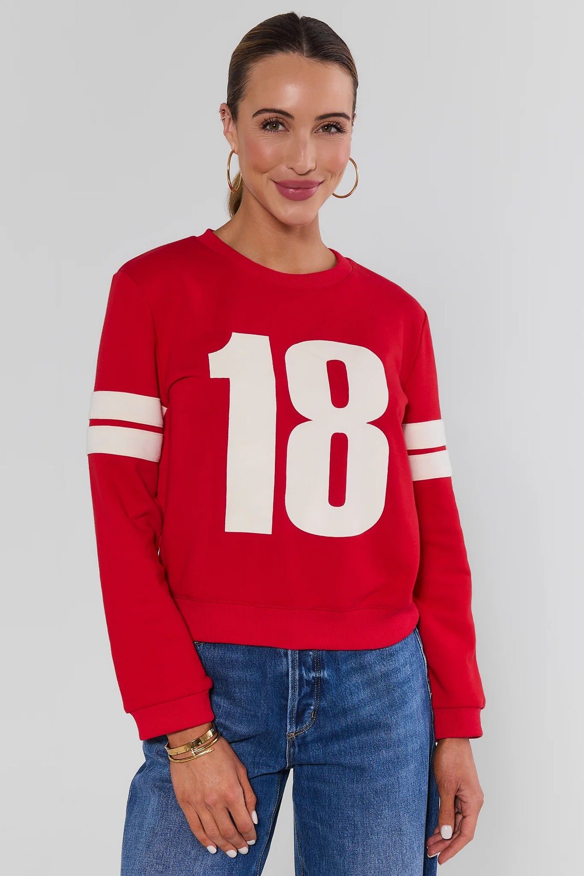 Red Varsity Number Pullover with white stripe sleeves and number 18 graphic, paired with jeans - Front View | Avara