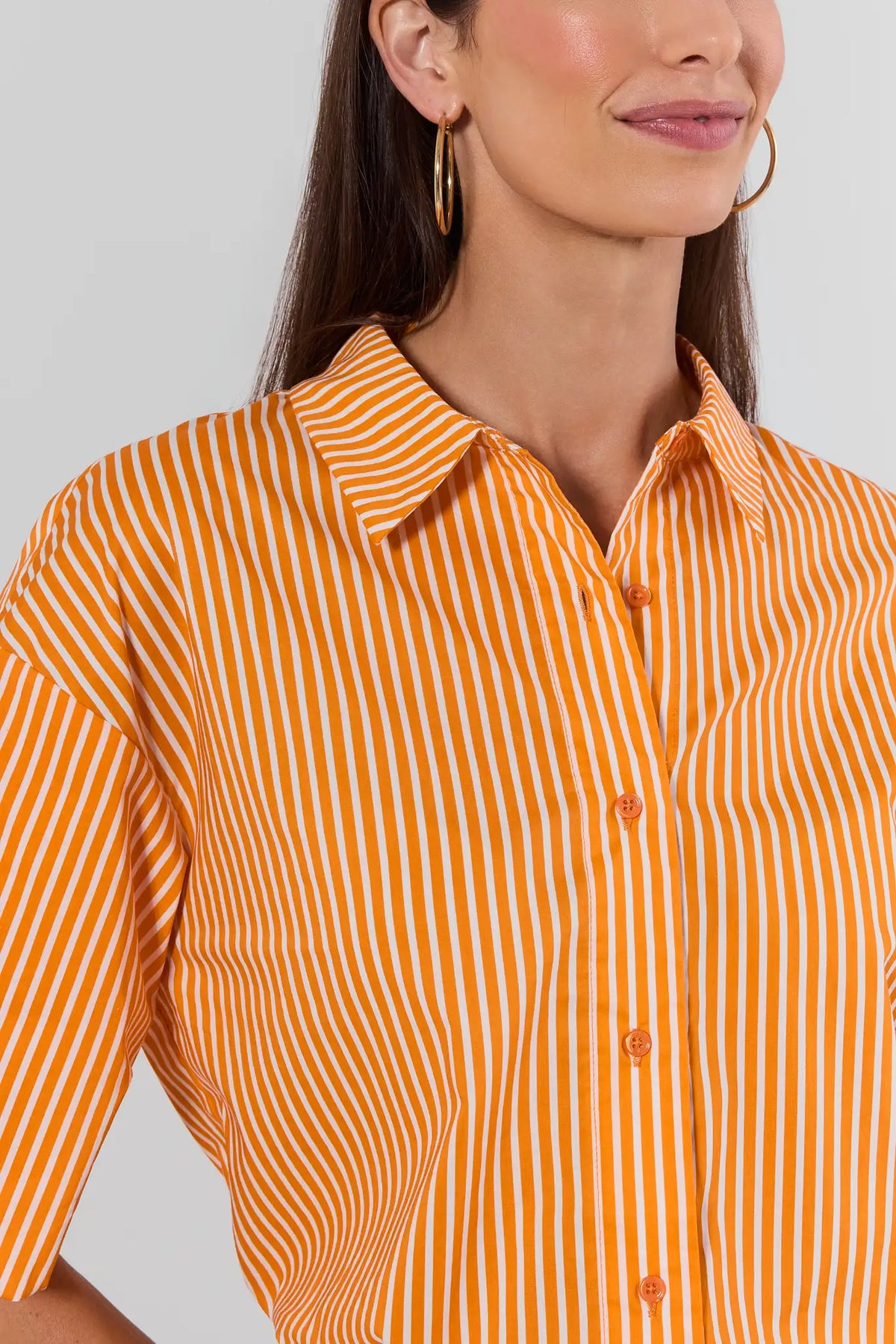 Close-up of orange and white striped button-up top showing spread collar and button detail, worn with gold hoops | Avara