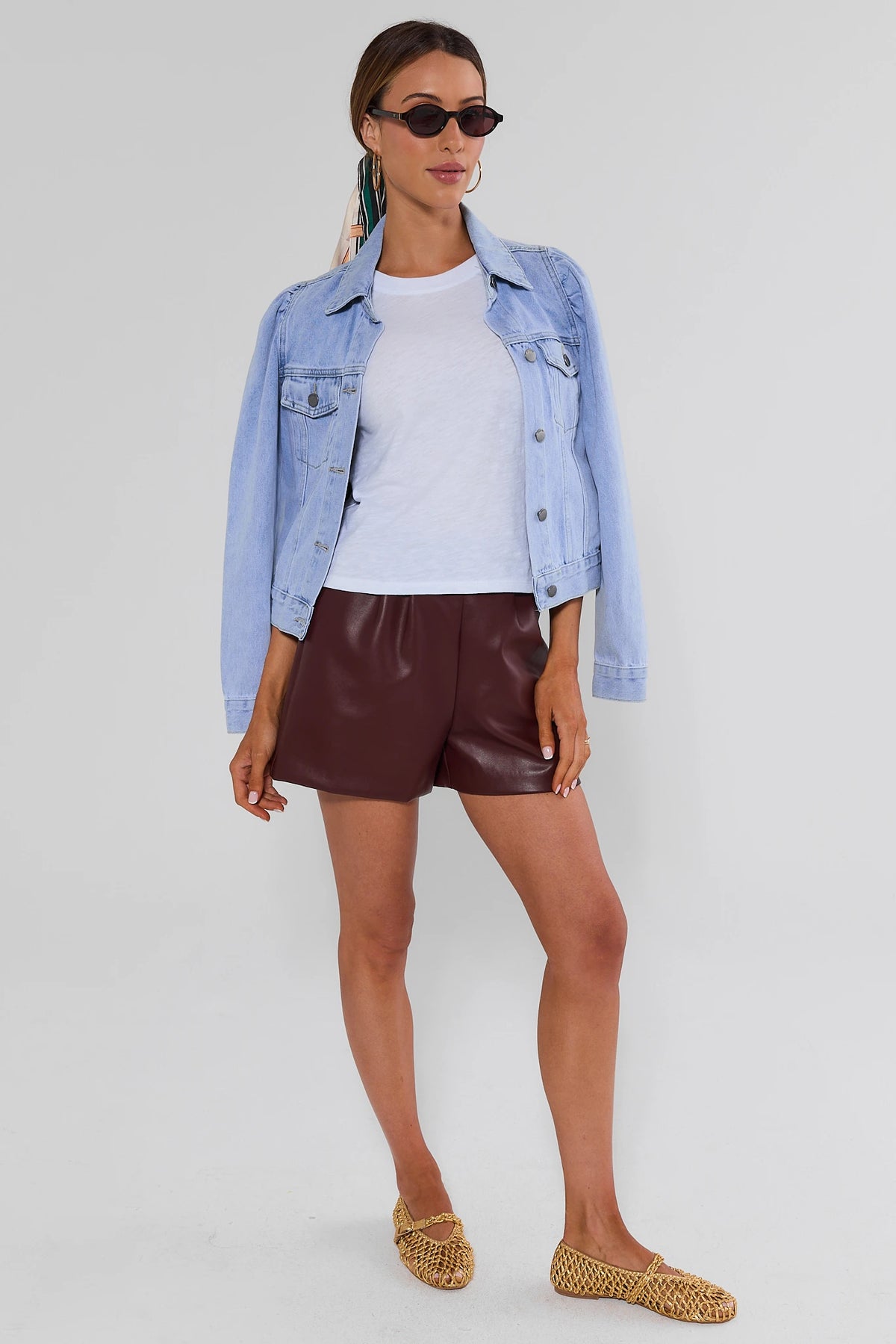 Burgundy leather shorts styled with denim jacket, white tee, and woven flats, full outfit front view | Avara
