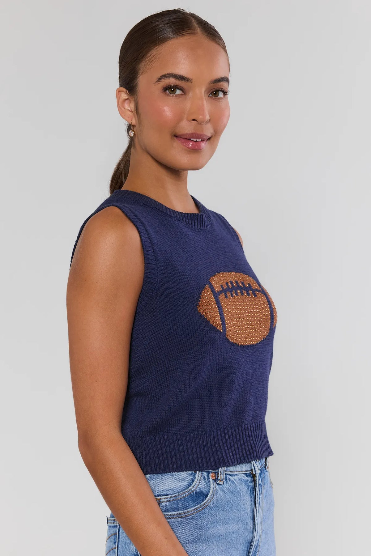 AJ Navy Football Sleeveless Knit Top showing rhinestone football graphic and ribbed hem, navy sleeveless knit - Side Profile | Avara