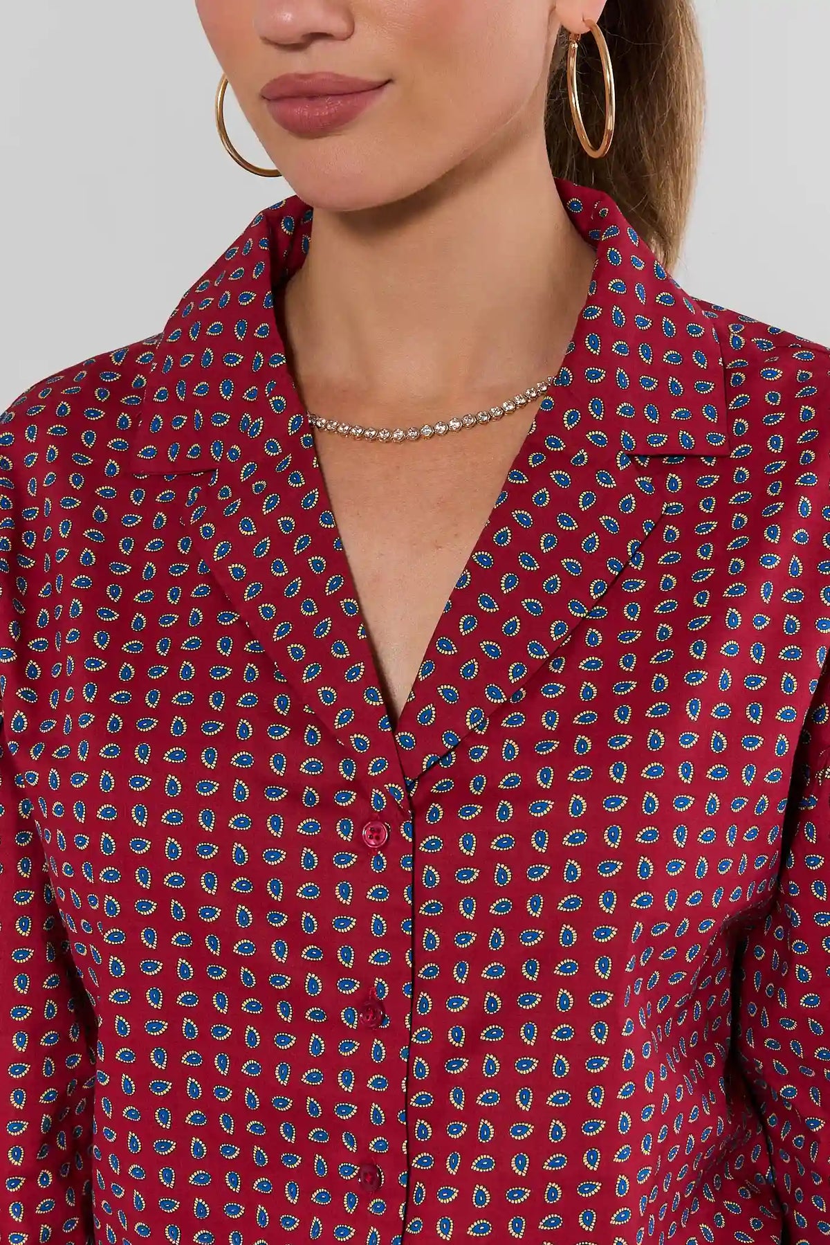 Maroon printed button-up top close-up showing notched collar, blue paisley print detail, and rhinestone necklace | Avara