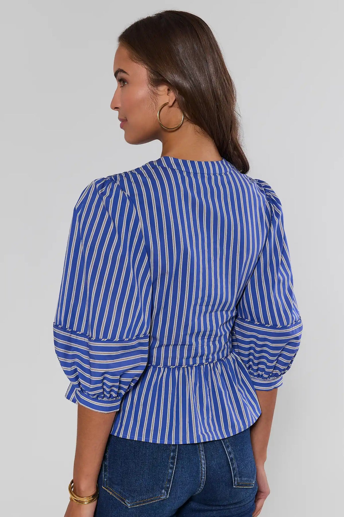 Blue striped peplum top back view showing gathered peplum hem and puff sleeves, paired with dark jeans | Avara