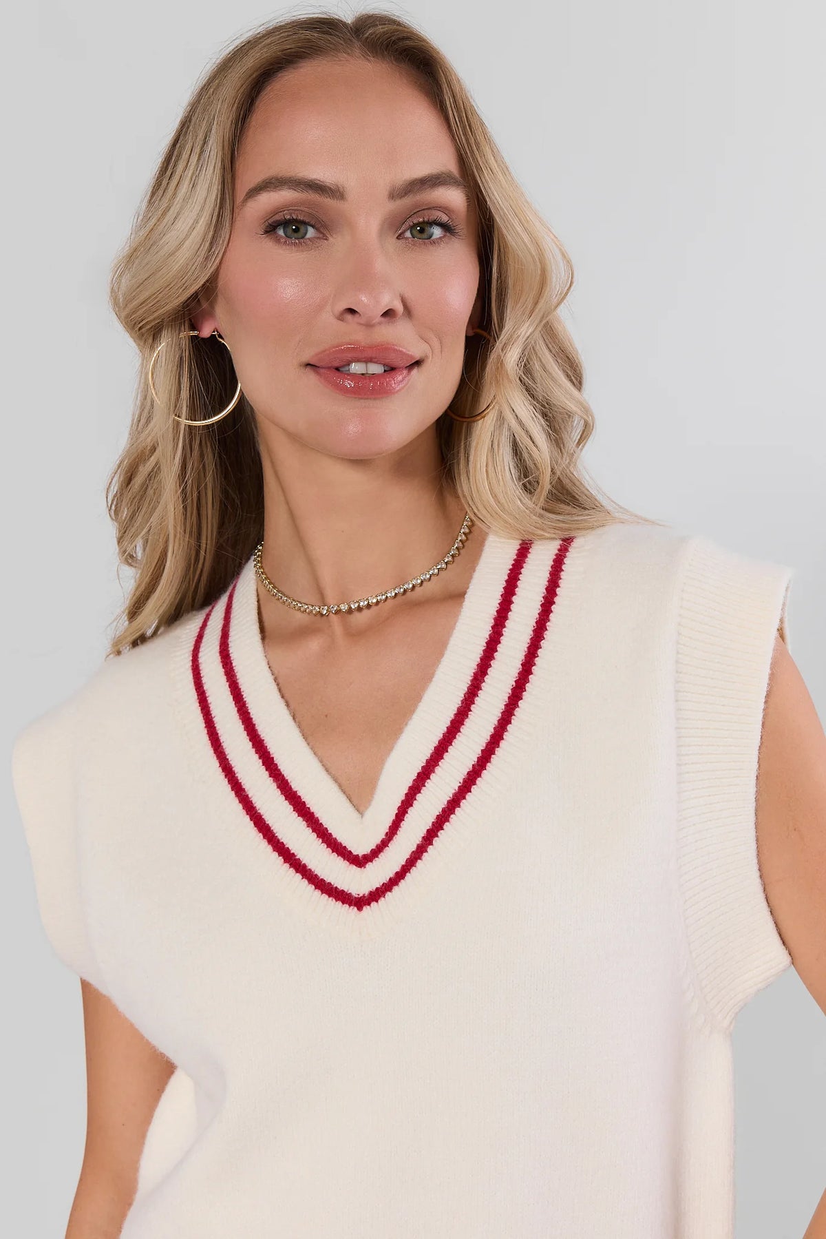 White contrast trim sweater vest with red V-neck stripe, gold hoops and necklace - Neckline Detail | Avara