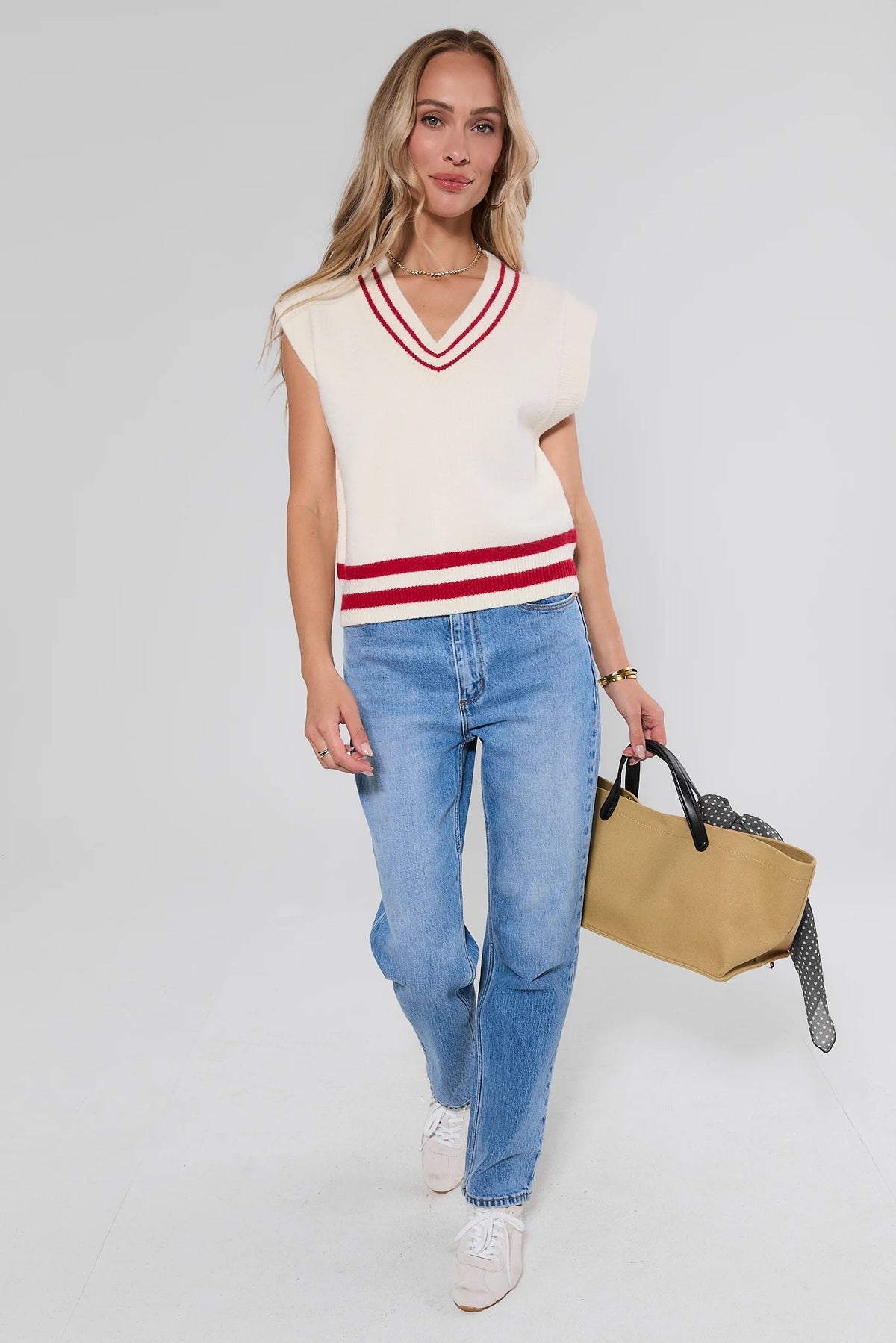 White preppy sweater vest with red stripe trim styled with jeans, white sneakers, and tan tote - Full Body View | Avara