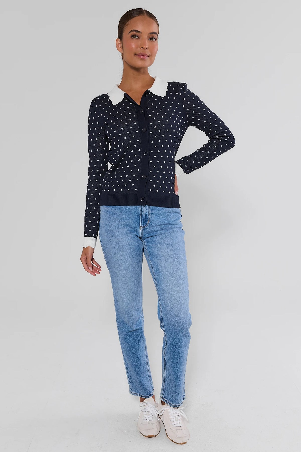 Women's navy polka dot cardigan sweater styled with light wash jeans and white sneakers - Full Length Front | Avara