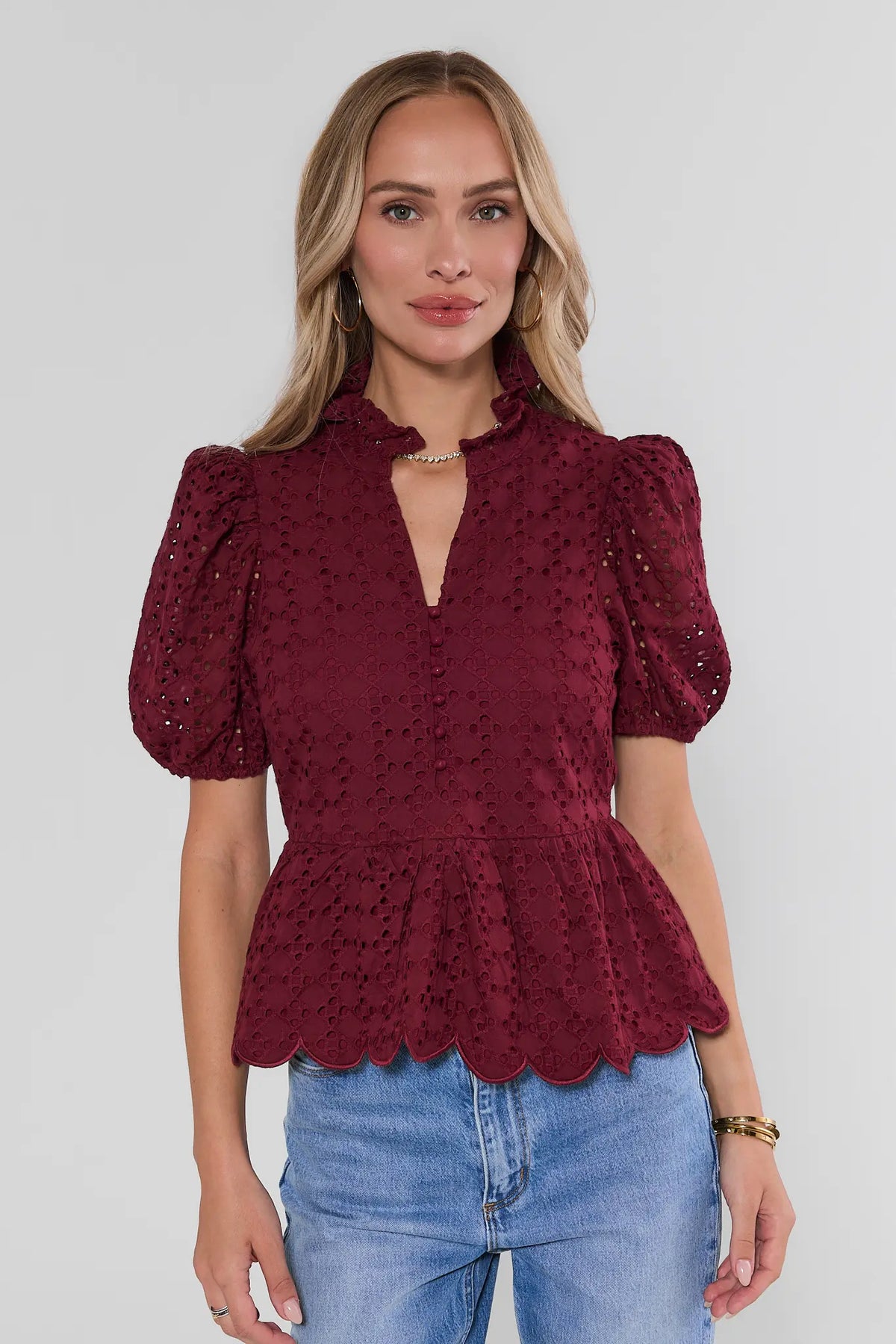 Maroon eyelet peplum top with puff sleeves, ruffle neckline, and scalloped hem, paired with blue jeans - Front View | Avara