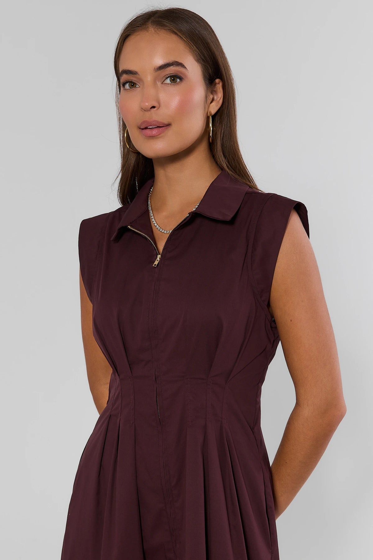 Dark burgundy zip-up midi dress with collared neckline and pleated waist, close-up detail on model | Avara