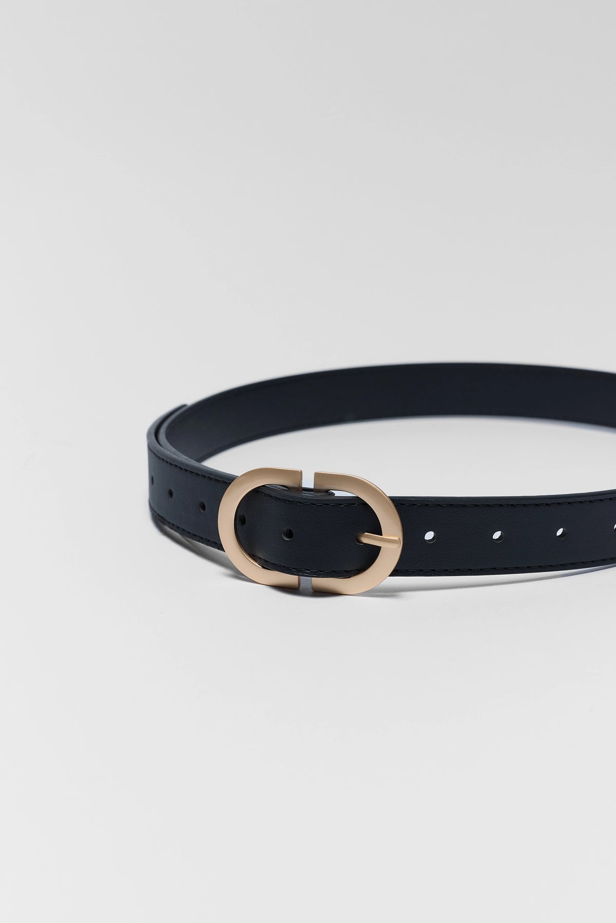 Black Faux Leather Belt coiled to show gold-tone oval buckle hardware close-up detail | Avara