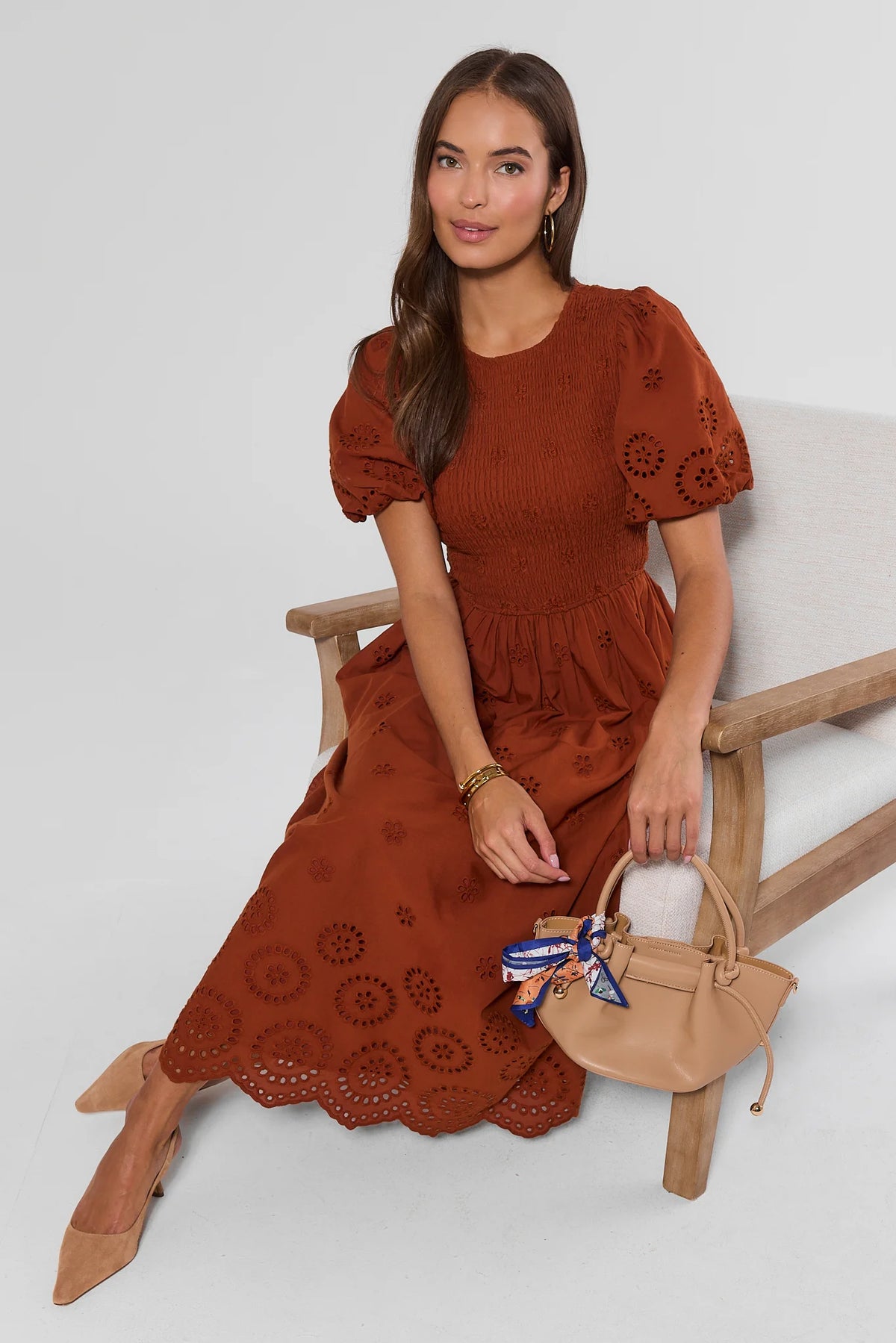 Rust Cotton Eyelet Smocked Midi Dress - Seated Lifestyle View with Tan Heels | Avara