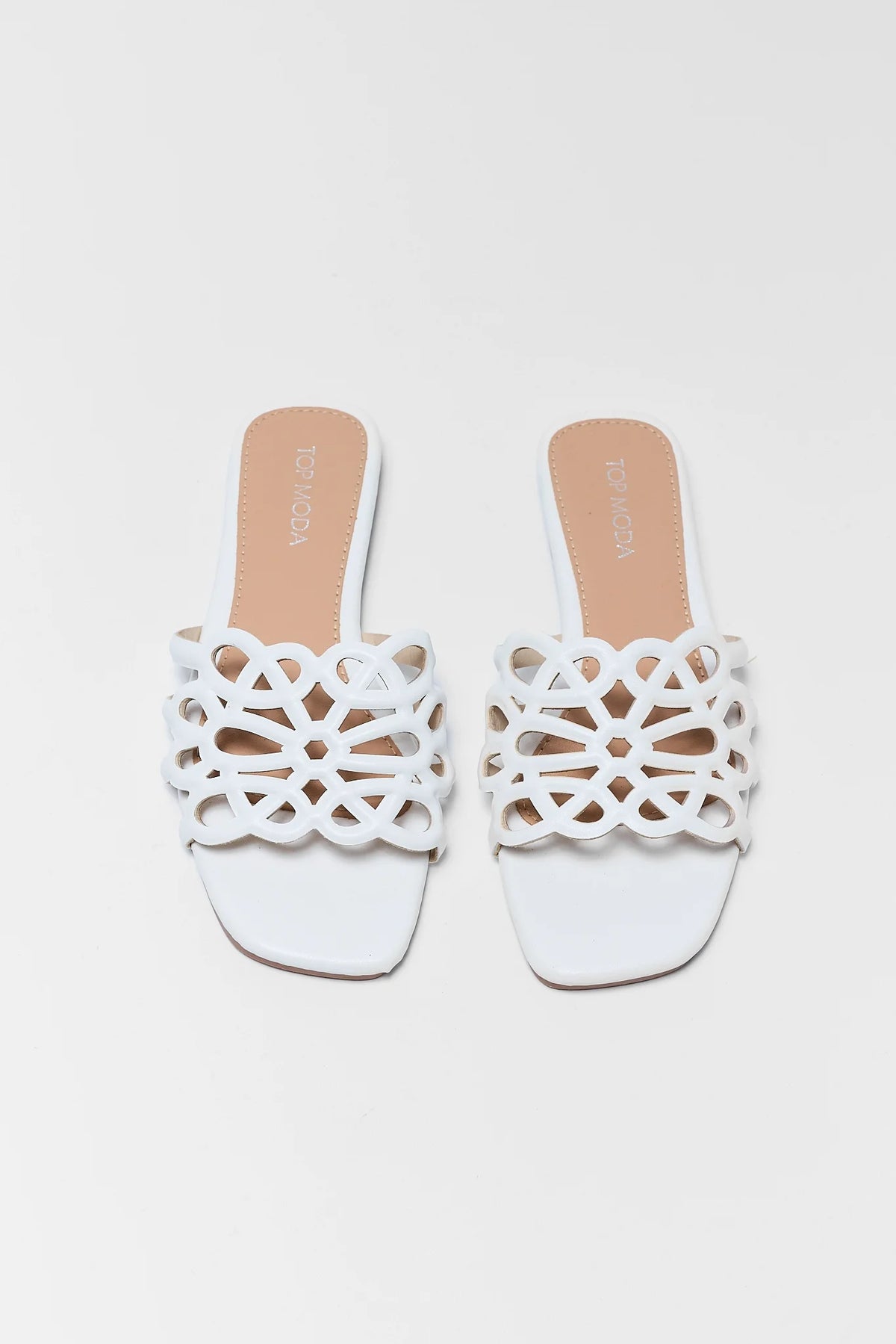 White cutout floral slide sandals styled on sand with woven palm fan - resort flat lay | Avara