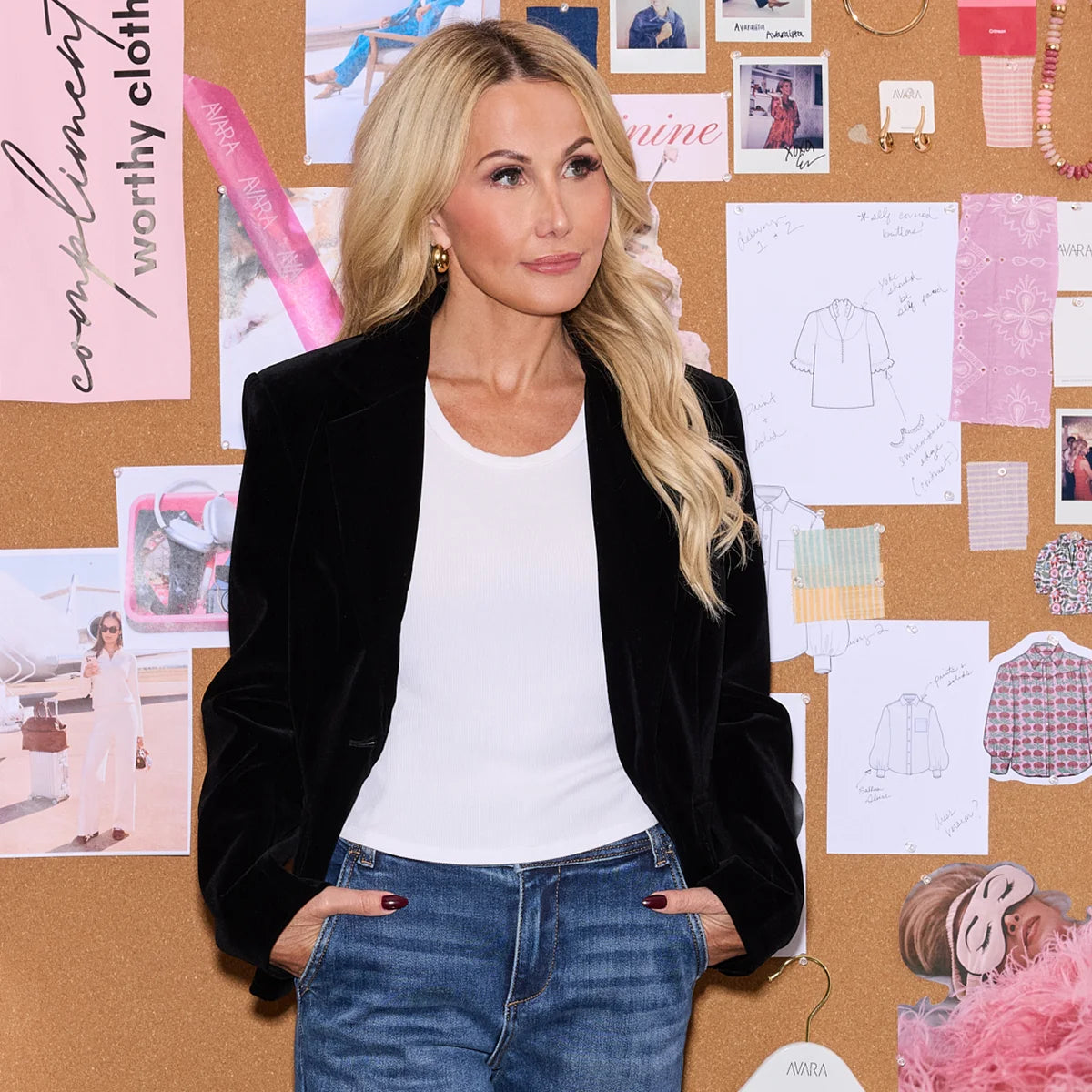 Woman in black blazer and white shirt standing in front of a corkboard with various images and notes.