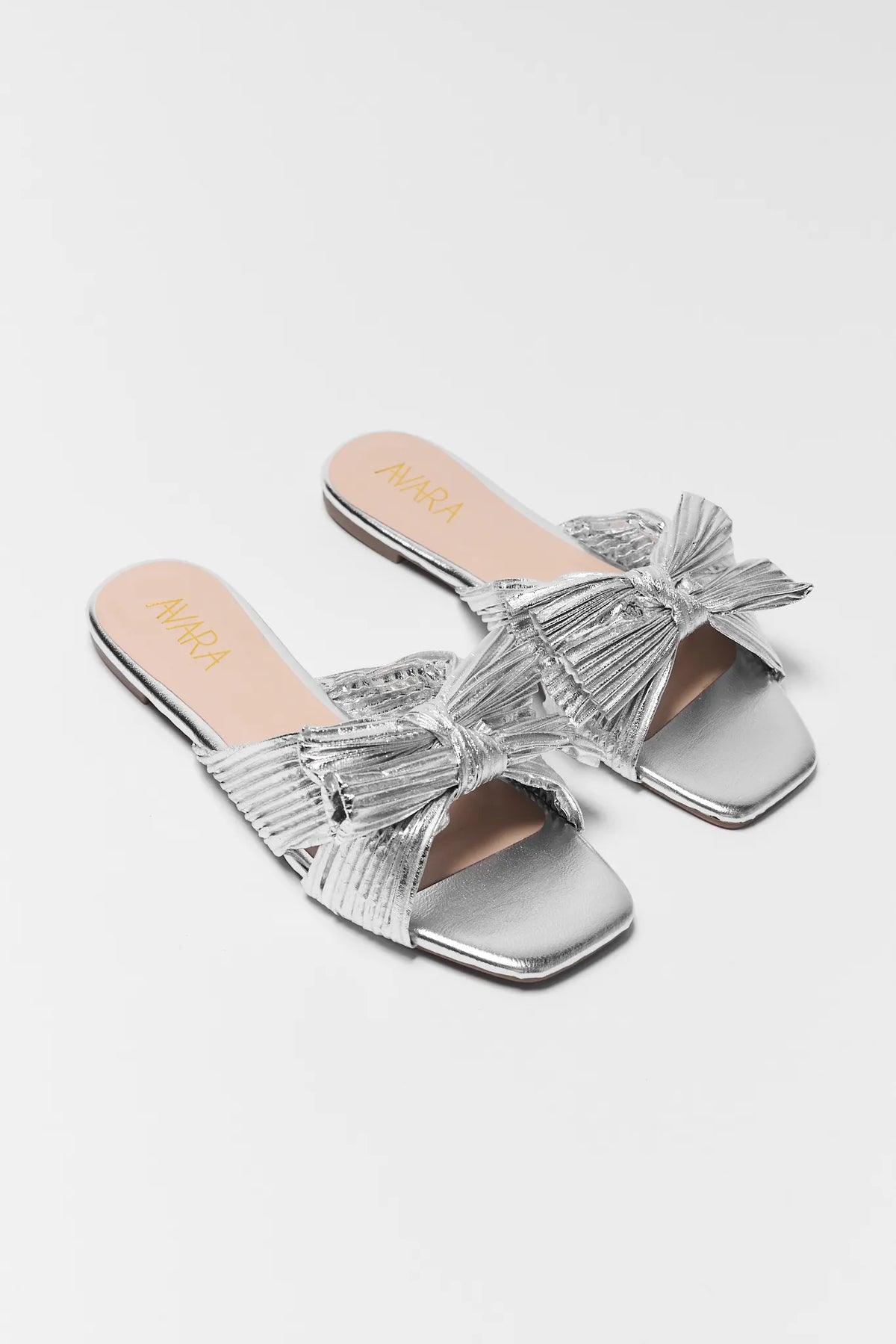 Silver metallic slide sandals with knot bow detail, angled pair view on light background | Avara