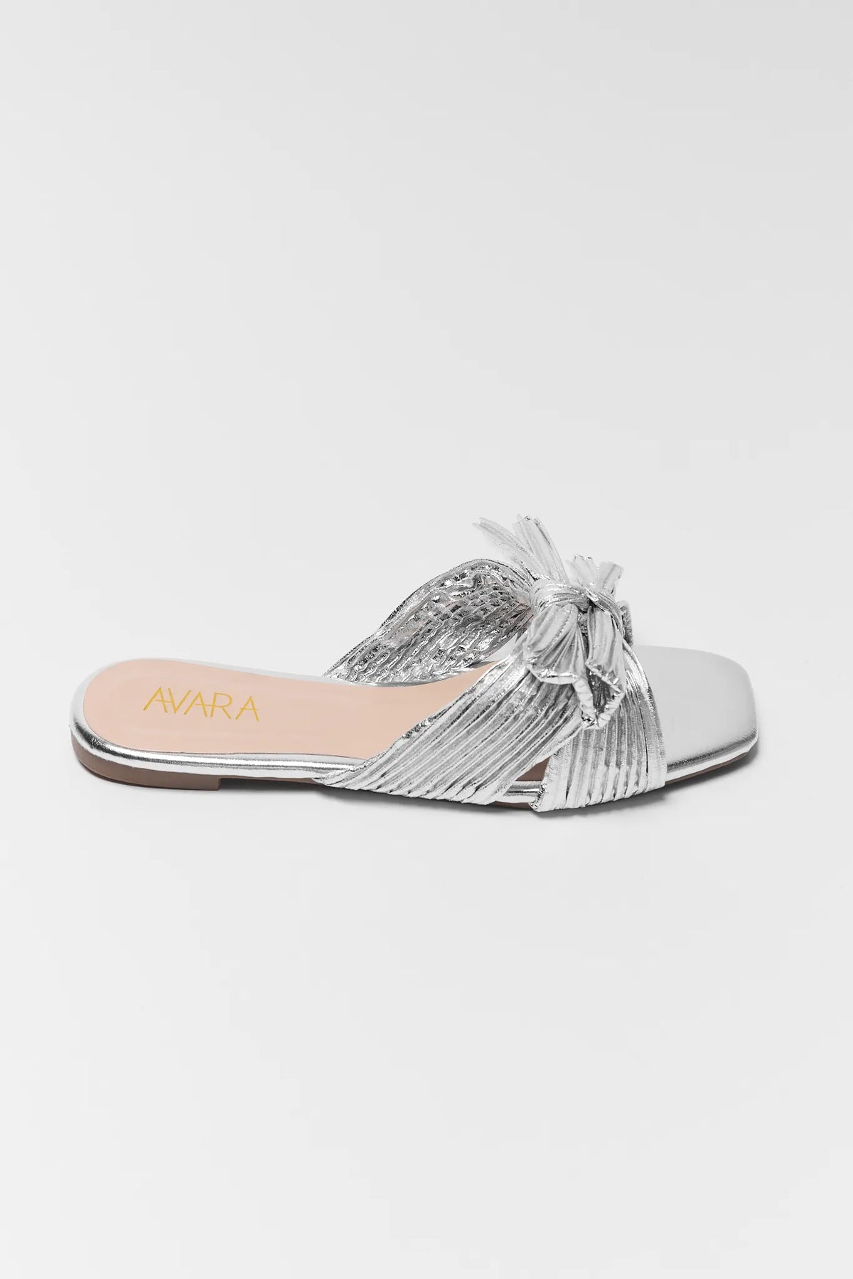 Silver metallic slip-on slide sandal with pleated knot bow, side profile view | Avara
