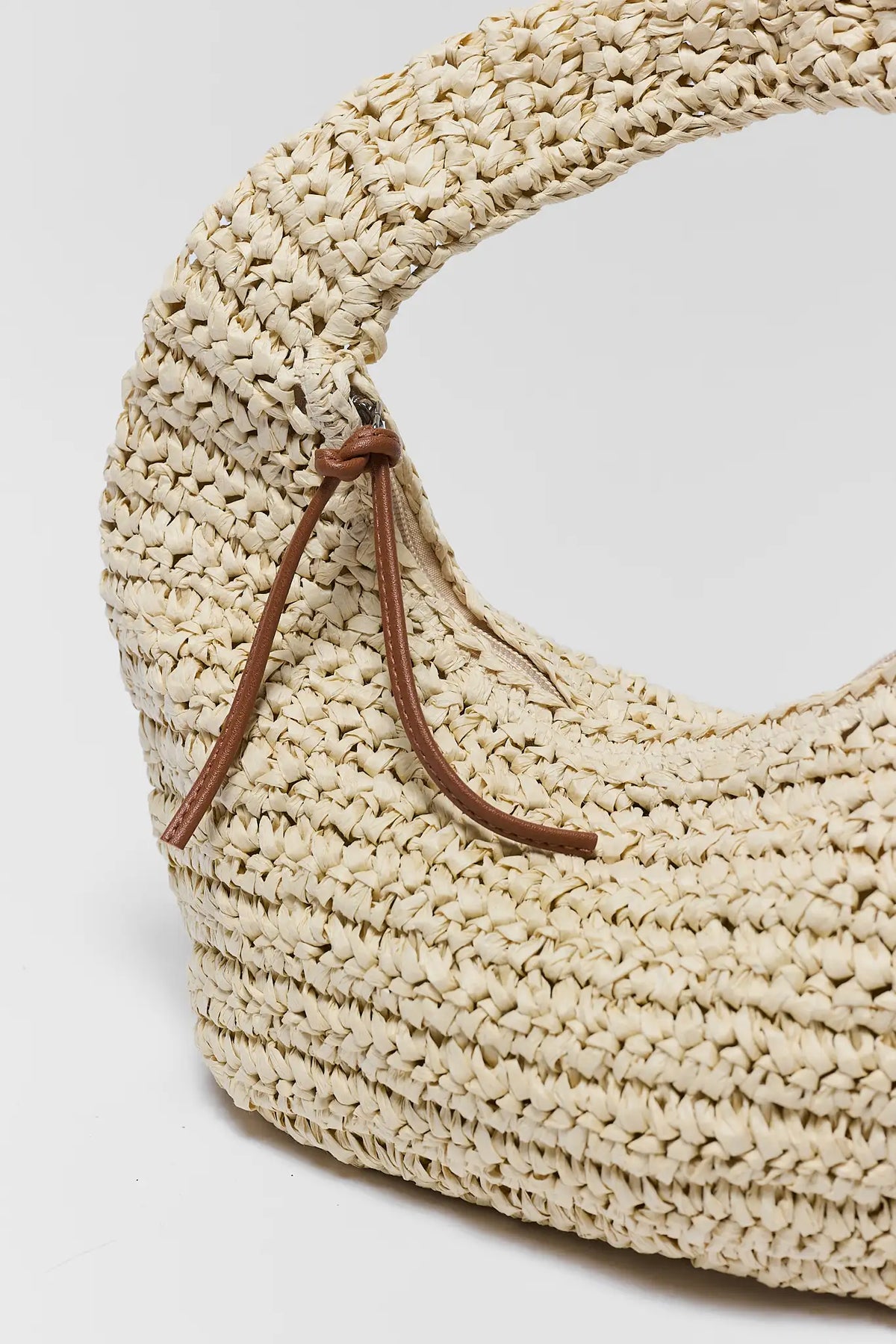 Beige woven bag with a brown strap on a light gray background