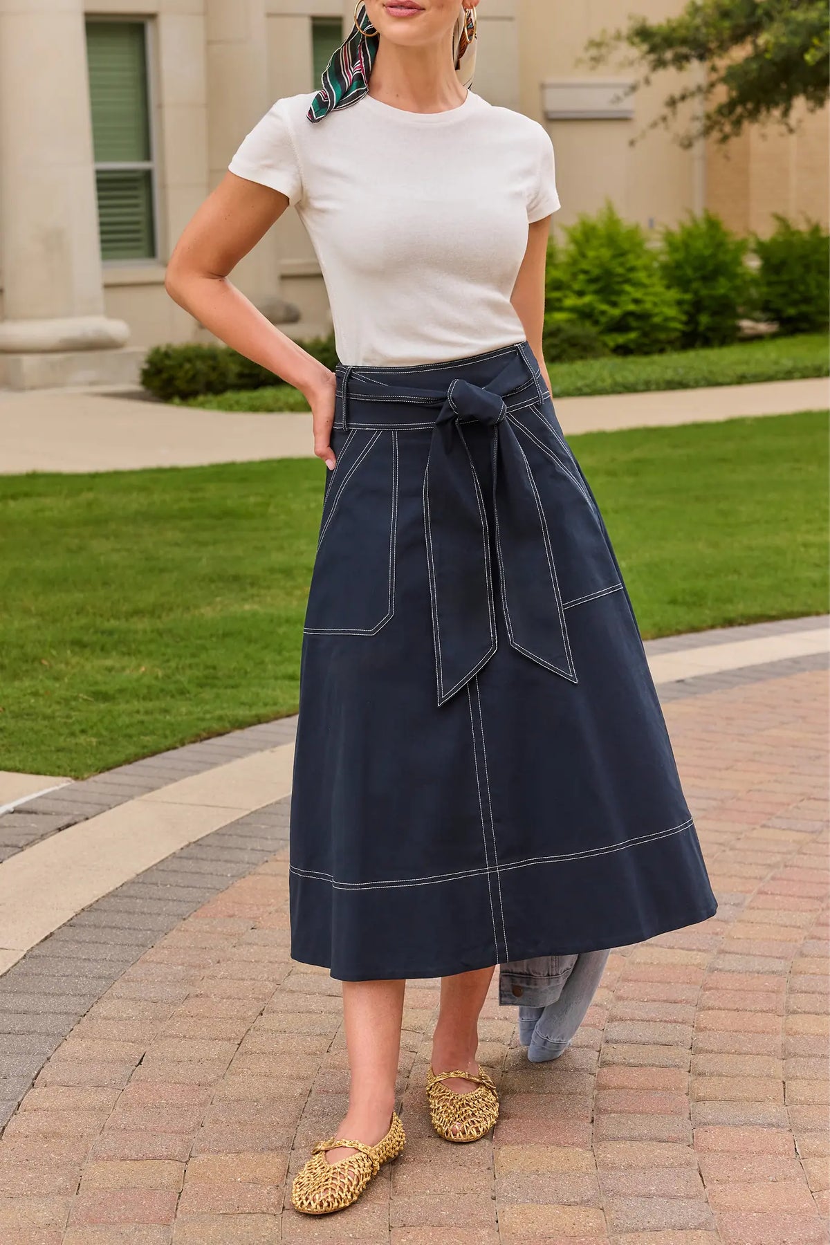 Charlotte Tie Waist Midi Skirt in navy with white contrast stitching, styled with white tee and woven flats outdoors | Avara